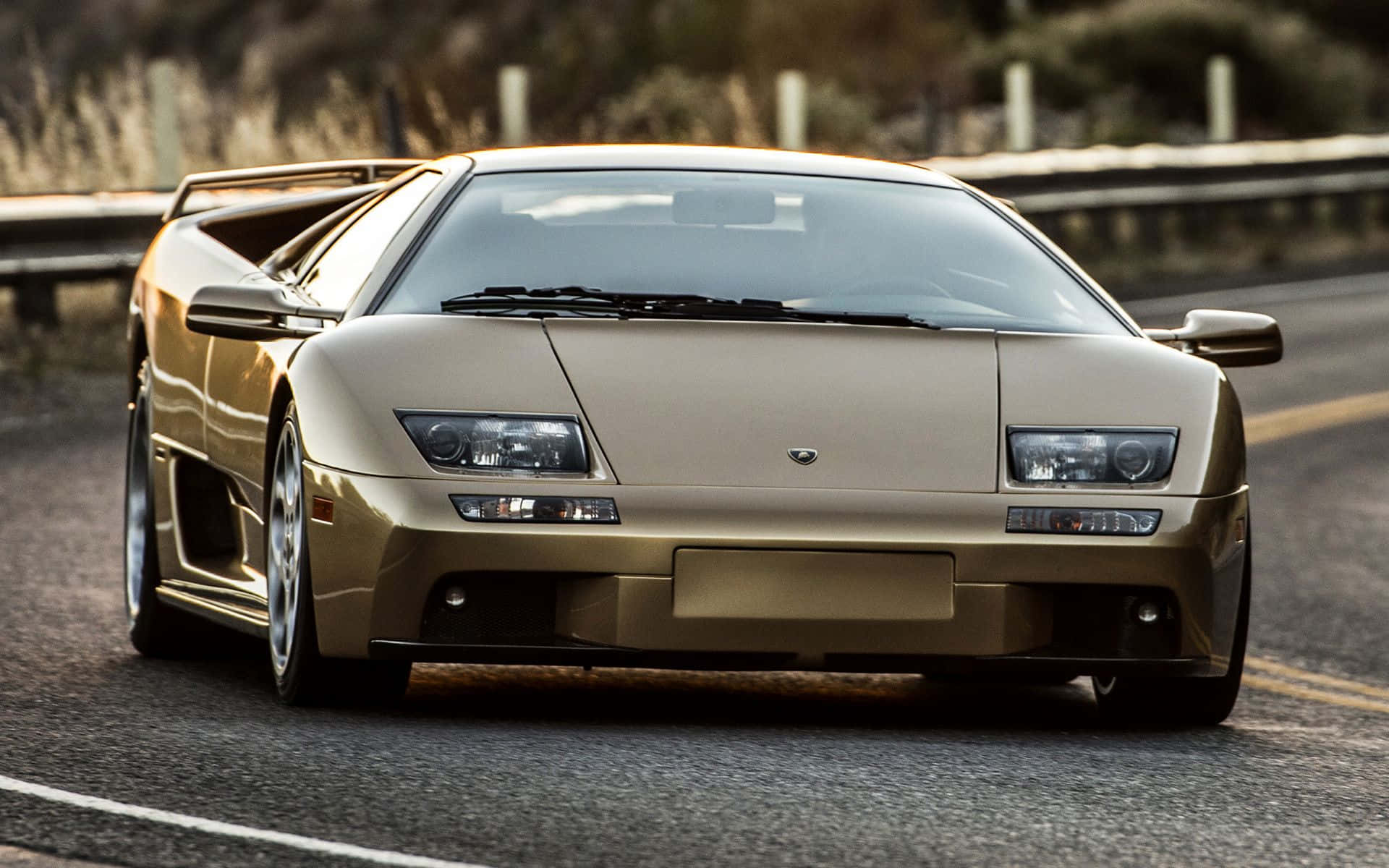 Lamborghini Diablo 桌布 壁紙 — 一架金色林寶堅尼Diablo跑車在陽光明媚的高速公路上閃閃發光，路邊植物模糊。