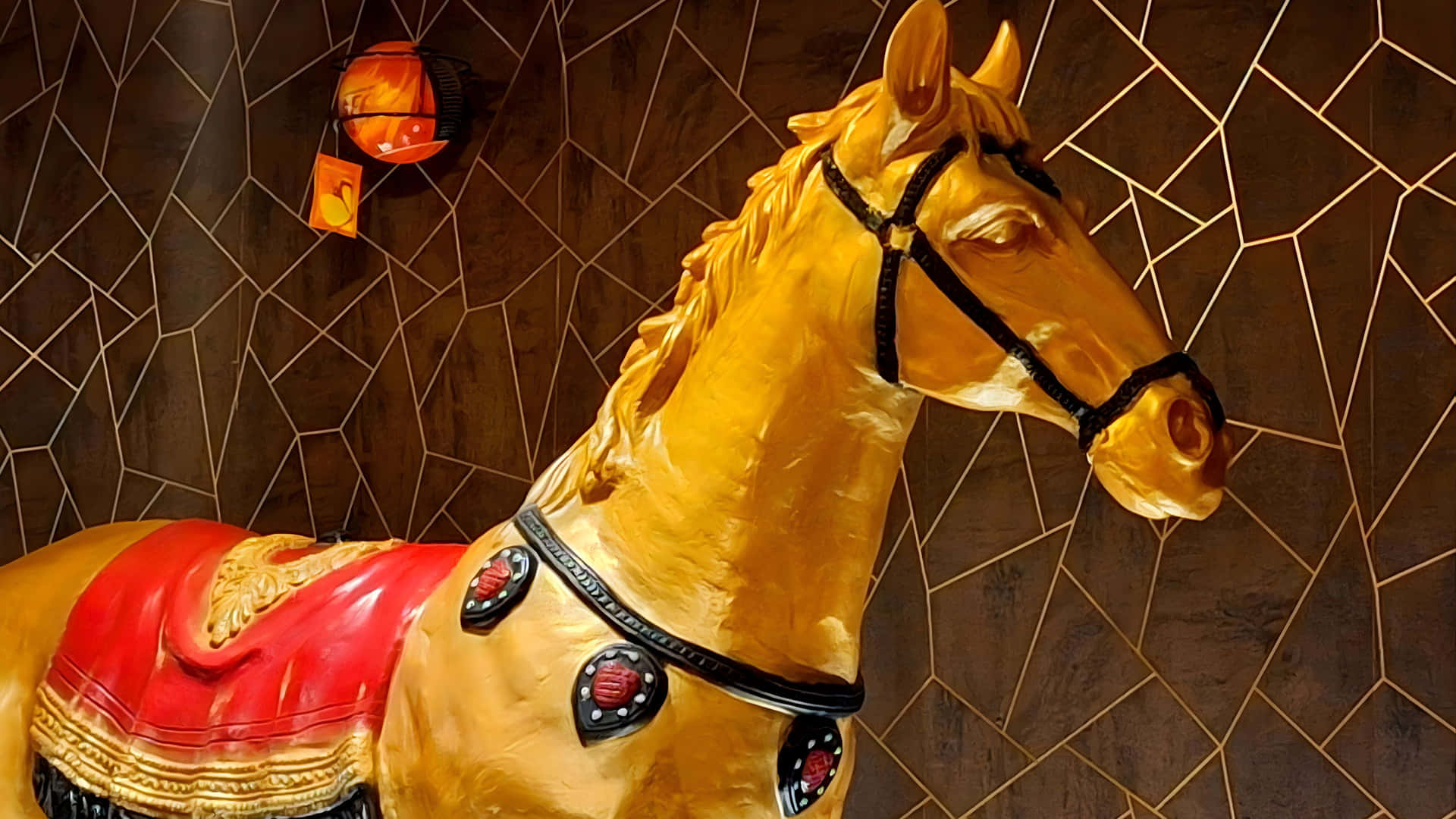  壁紙 — 金色馬雕像飾有紅色馬鞍和黑色飾邊，在溫暖燈光下立於深色幾何瓷磚牆前。