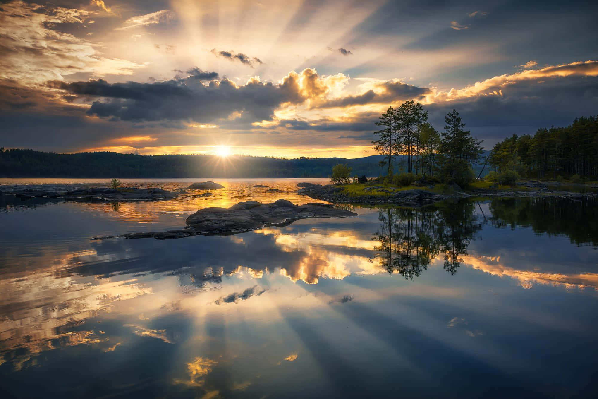 Sunset Reflection 桌布 壁紙 — 金色陽光穿透雲層，映照在平靜的湖面上，反射出樹木和天空，呈現寧靜的黃昏景色。