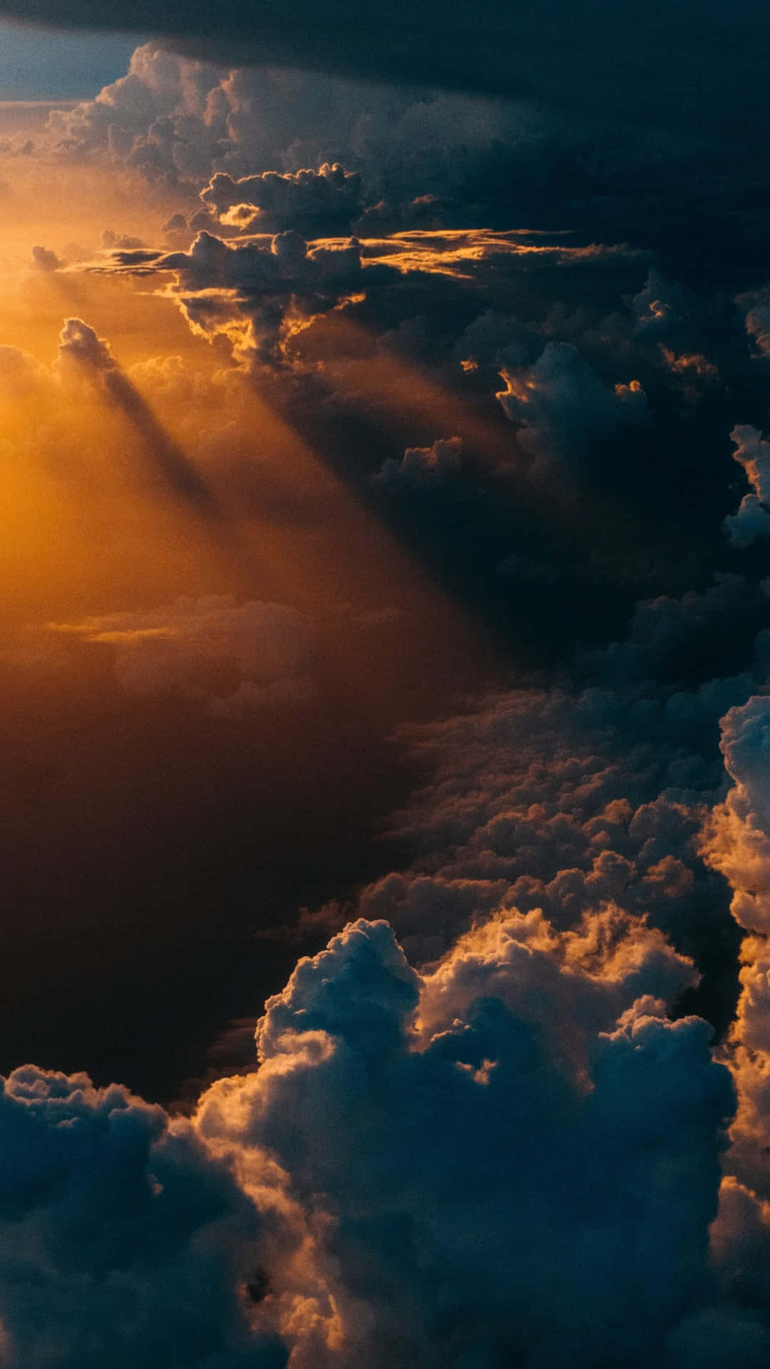  壁紙 — 金色陽光穿透戲劇性的雲層，從上方將溫暖的光線灑在廣闊的暴風雨天空上。