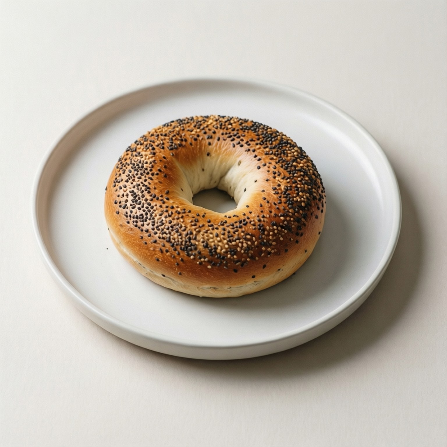 Minimalist Poppy Seed 壁紙 — 一個金黃色的百吉餅，上面撒有罌粟籽和芝麻，放在簡約的白色碟子中央，背景是柔和的米白色。