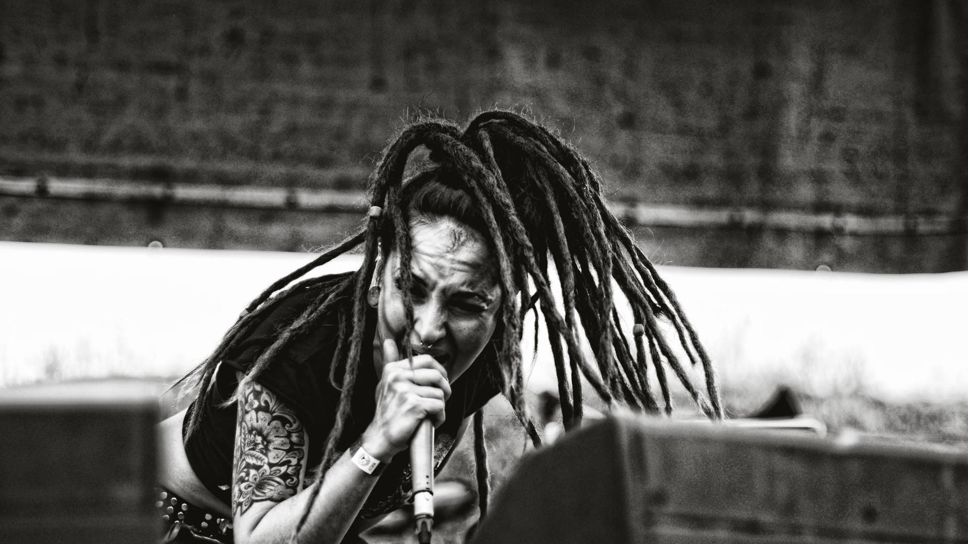 一位留著辮子、有紋身的音樂家在音樂會上熱情地對著麥克風唱歌。