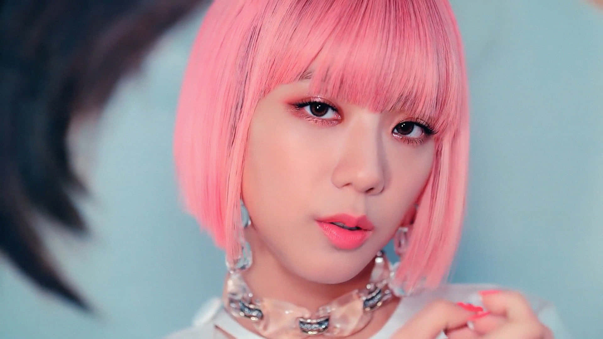 Jisoo BLACKPINK 粉紅髮簷銀項鍊 壁紙 — 一位年輕女性的特寫肖像，擁有充滿活力的粉紅色鮑伯頭和鮮豔妝容，背景是柔和的藍色。