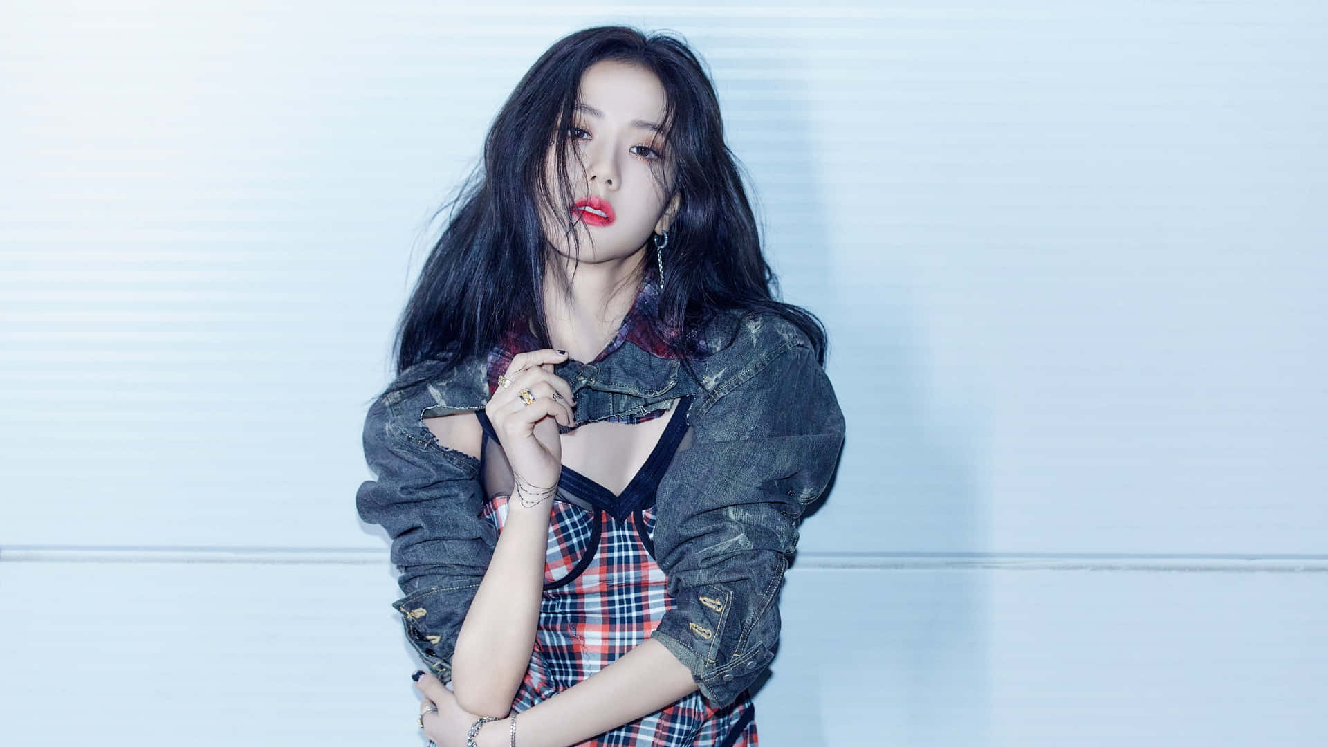 Jisoo BLACKPINK 野性凌亂髮型 壁紙 — 一位黑髮紅唇的年輕女性，身穿牛仔外套，在淺藍色鑲板牆前自信地擺姿勢。