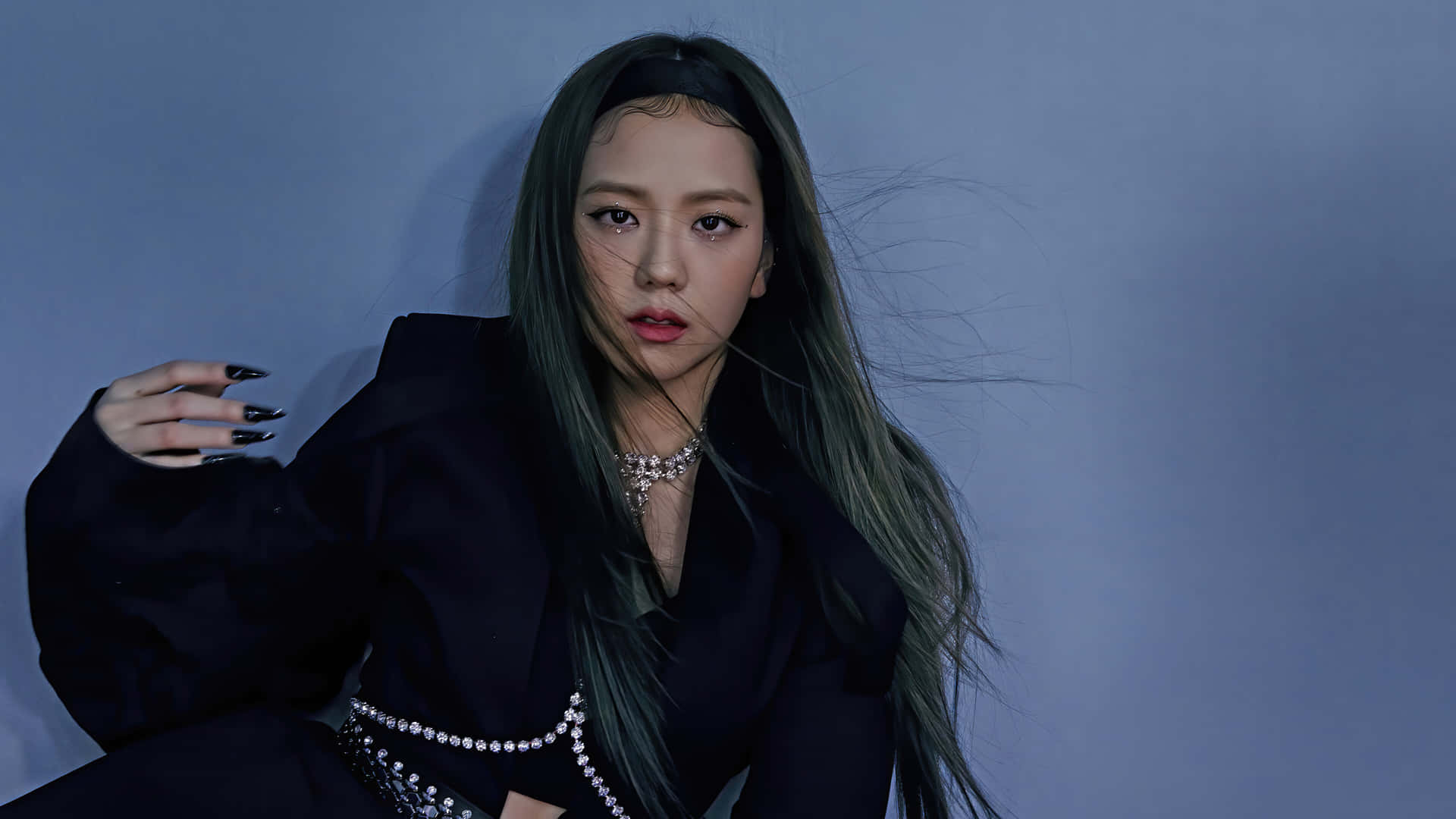 Jisoo BLACKPINK《How You Like That》暗黑風 壁紙 — 一位擁有長綠色頭髮和黑色指甲的女性，穿著黑色服裝，在清涼的藍色工作室背景前擺姿勢。