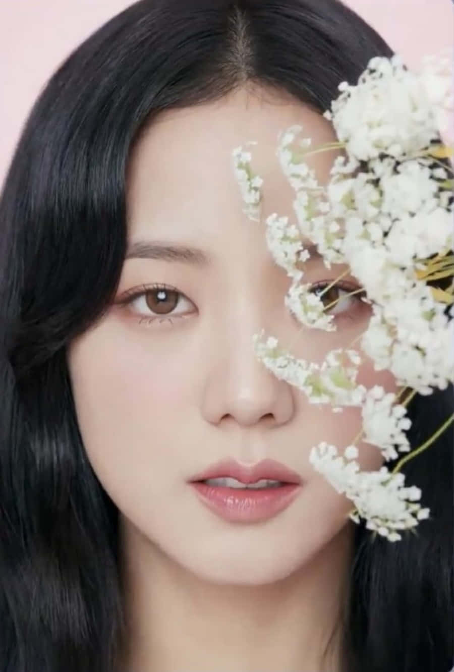 Jisoo 推廣她的最新熱門單曲 壁紙 — 一個特寫肖像，一位深色頭髮、妝容柔和的女人，部分被精緻的白花遮蓋，背景是淡粉色。
