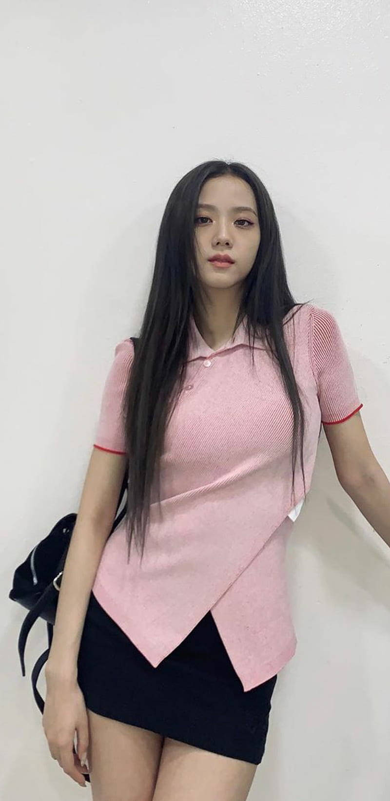年輕女性穿粉紅Polo和黑裙靠白牆
