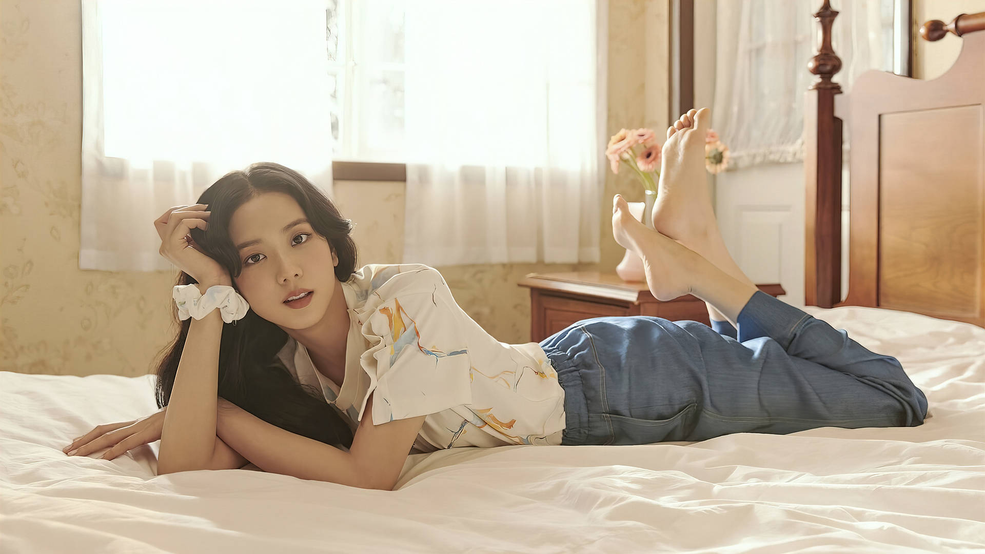 Jisoo 躺床姿勢 BLACKPINK 桌面壁紙 壁紙 — 一位年輕女性在陽光明媚的舒適臥室床上放鬆，赤腳且神情輕鬆，溫柔地凝視著相機。