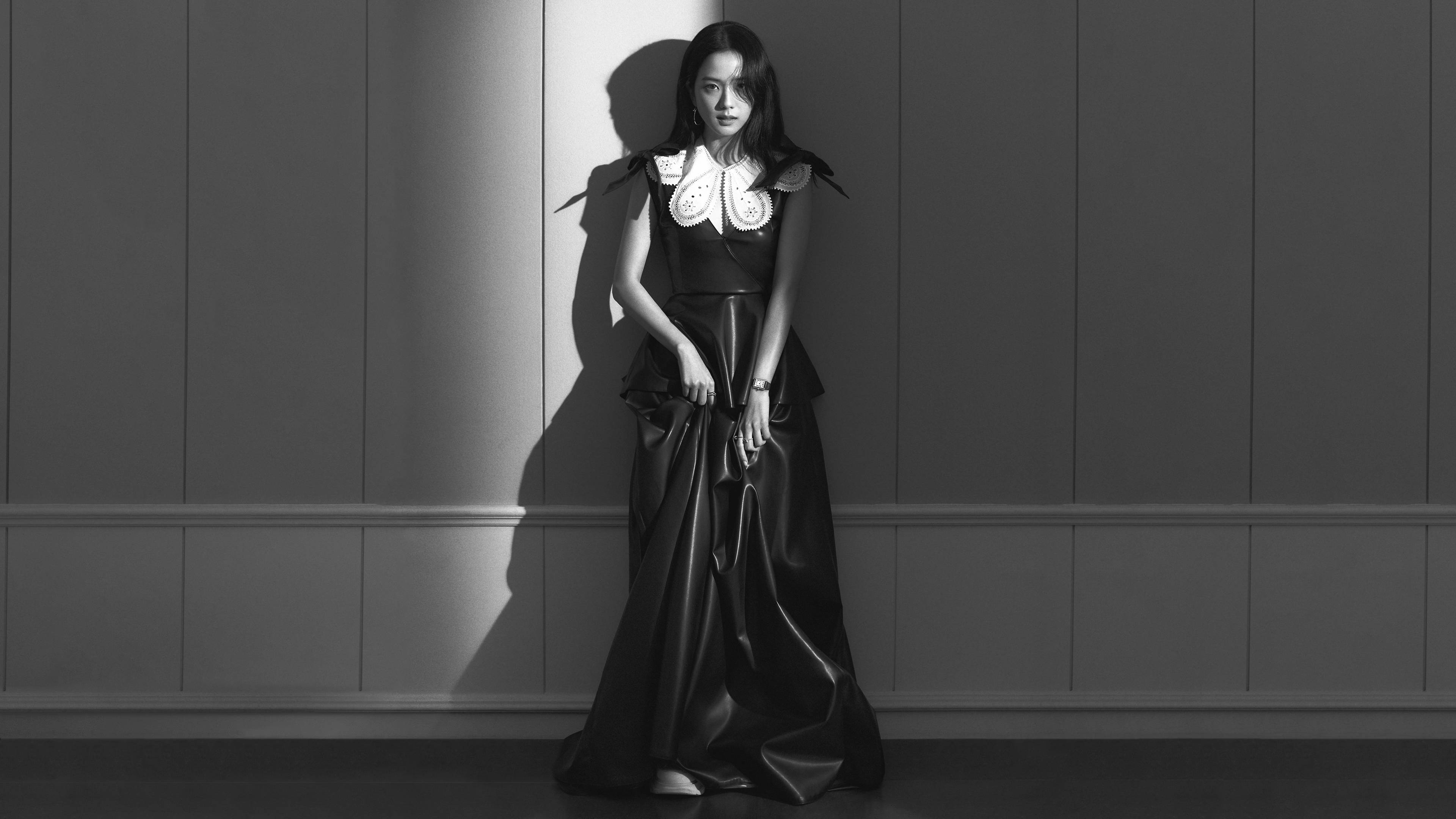 Jisoo 黑色禮服黑白風格 BLACKPINK 桌面壁紙 壁紙 — 一位身穿戲劇性黑色長裙、搭配白色蕾絲領口的女性，靠著鑲板牆站立，沐浴在強烈的明暗對比光線中。