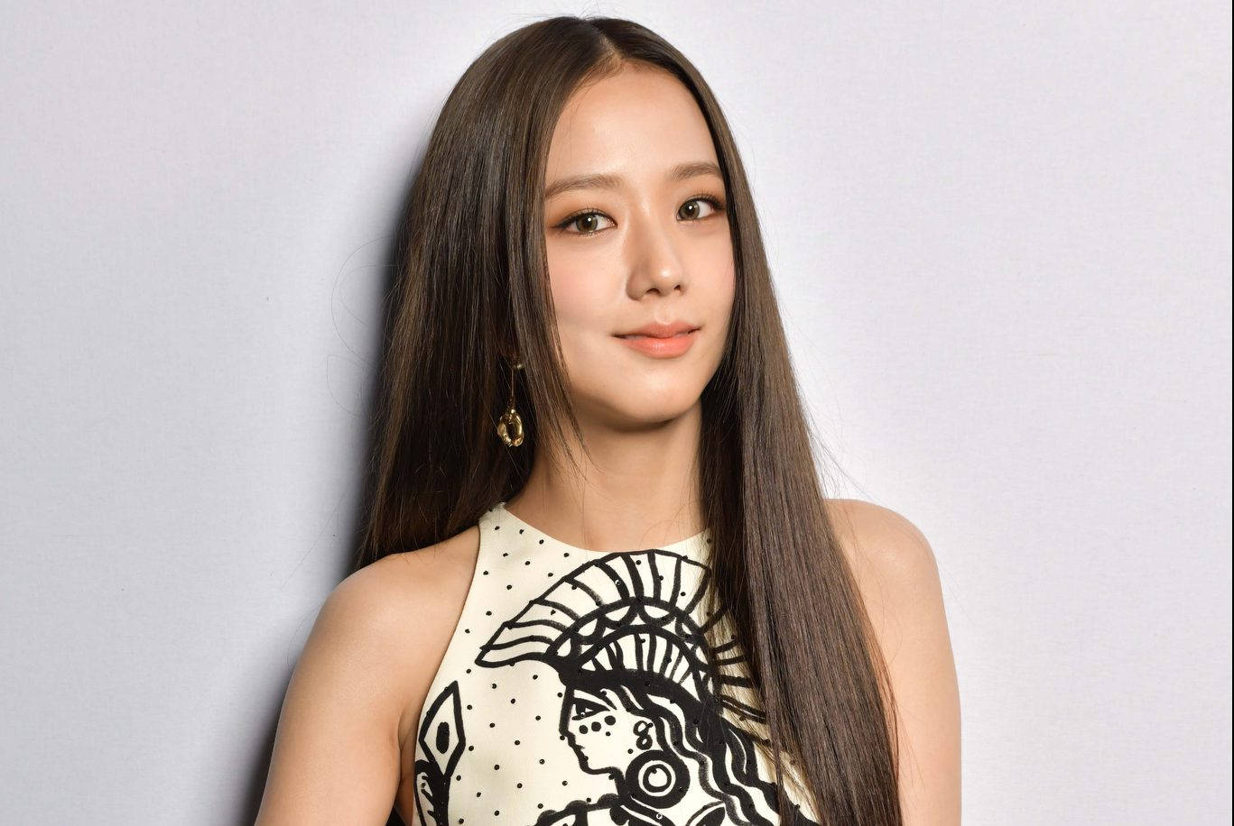 Jisoo巴黎時裝週 壁紙 — 一位年輕女性，長長的黑髮，穿著帶有黑色部落圖案的奶油色上衣和金色耳環，背景是純灰色。