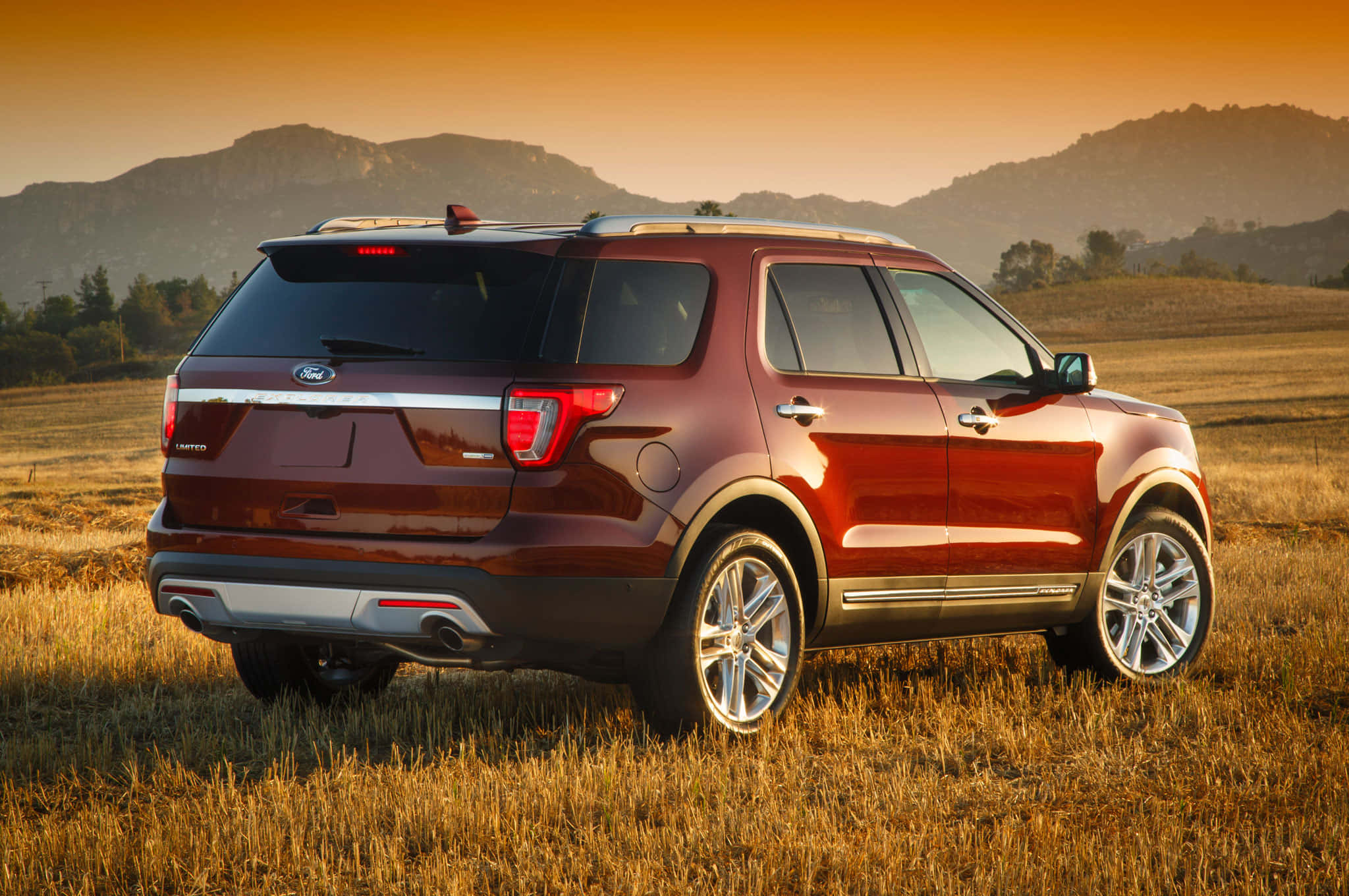 Ford Explorer 桌布 壁紙 — 一架酒紅色福特探險者SUV停在日落時分的金色田野中，背景有山脈。