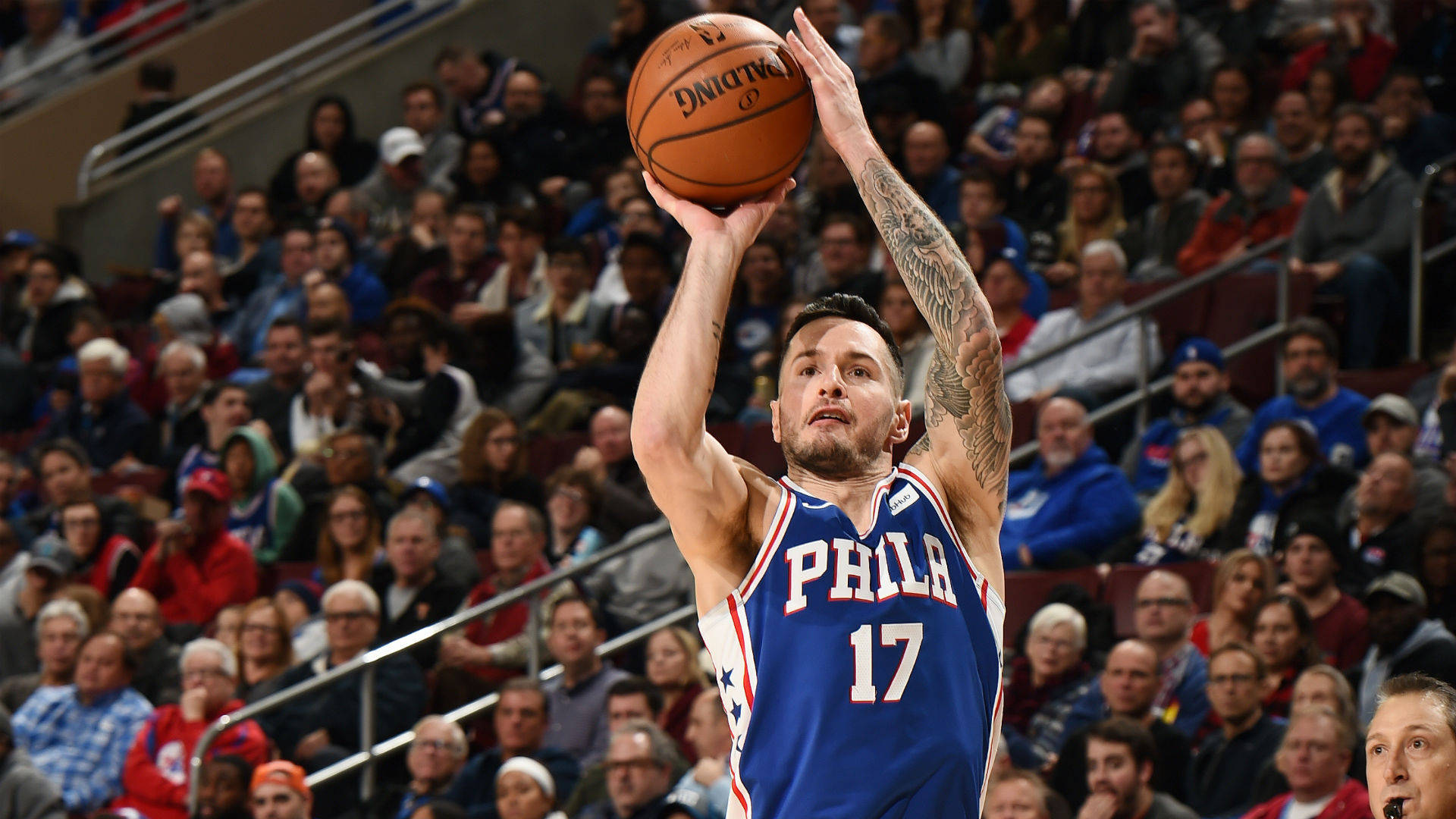 Jj Redick 火箭三分投籃 壁紙 — 一名身穿藍色 'PHILA' 球衣的籃球運動員，手臂上有可見的紋身，在擠滿觀眾的場館中投籃。