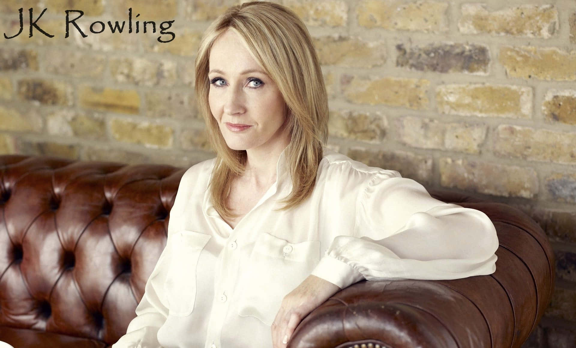 J K Rowling 桌布 壁紙 — JK羅琳身穿白色襯衫，平靜地坐在一張棕色皮革簇絨沙發上，背景是質樸的磚牆。