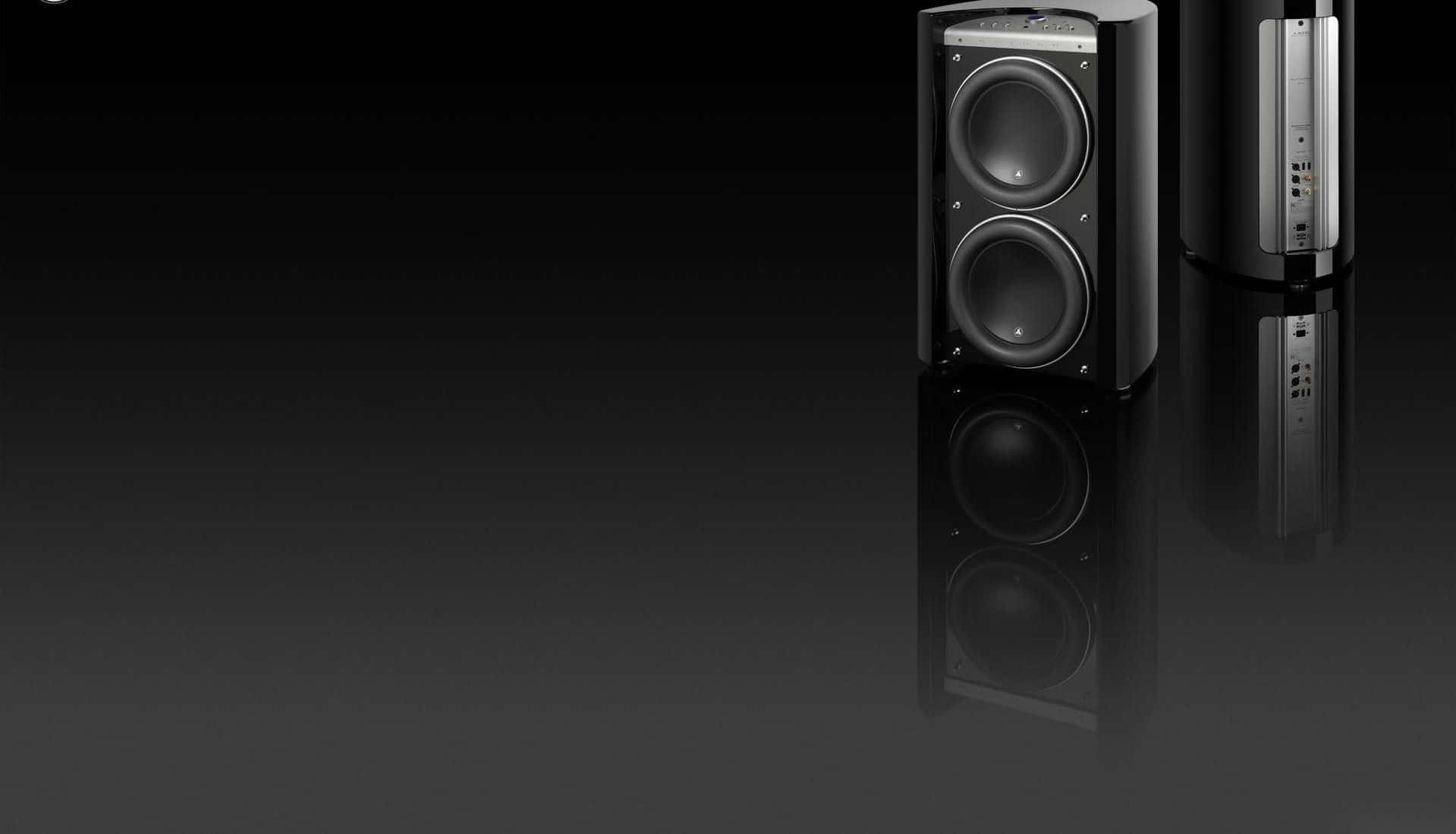 極簡風格 JL Audio Gotham 黑色喇叭 壁紙 — 兩款時尚的黑色落地喇叭，帶有銀色點綴，立於反射的深色表面上，背景為漸變黑色。