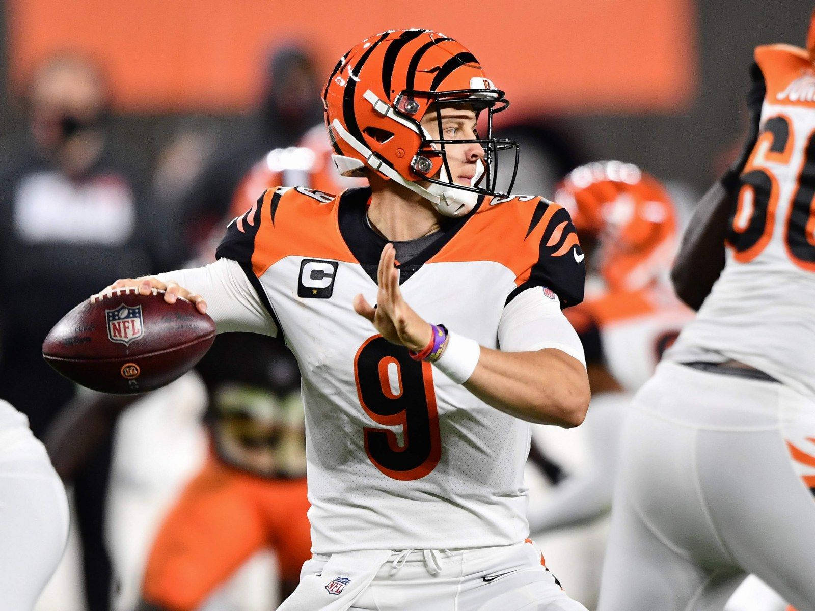 Joe Burrow Bengals 四分衛 壁紙 — 一位身穿橙黑色球衣的辛辛那提猛虎四分衛在夜間比賽中準備擲出橄欖球。