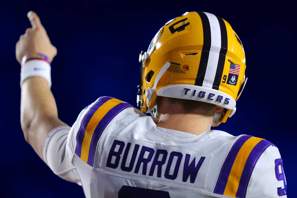 Joe Burrow 後視圖 壁紙 — 一名身穿白色、紫色和金色球衣、背後印有「BURROW」的美式足球四分衛在球場燈光下豎起大拇指慶祝勝利。