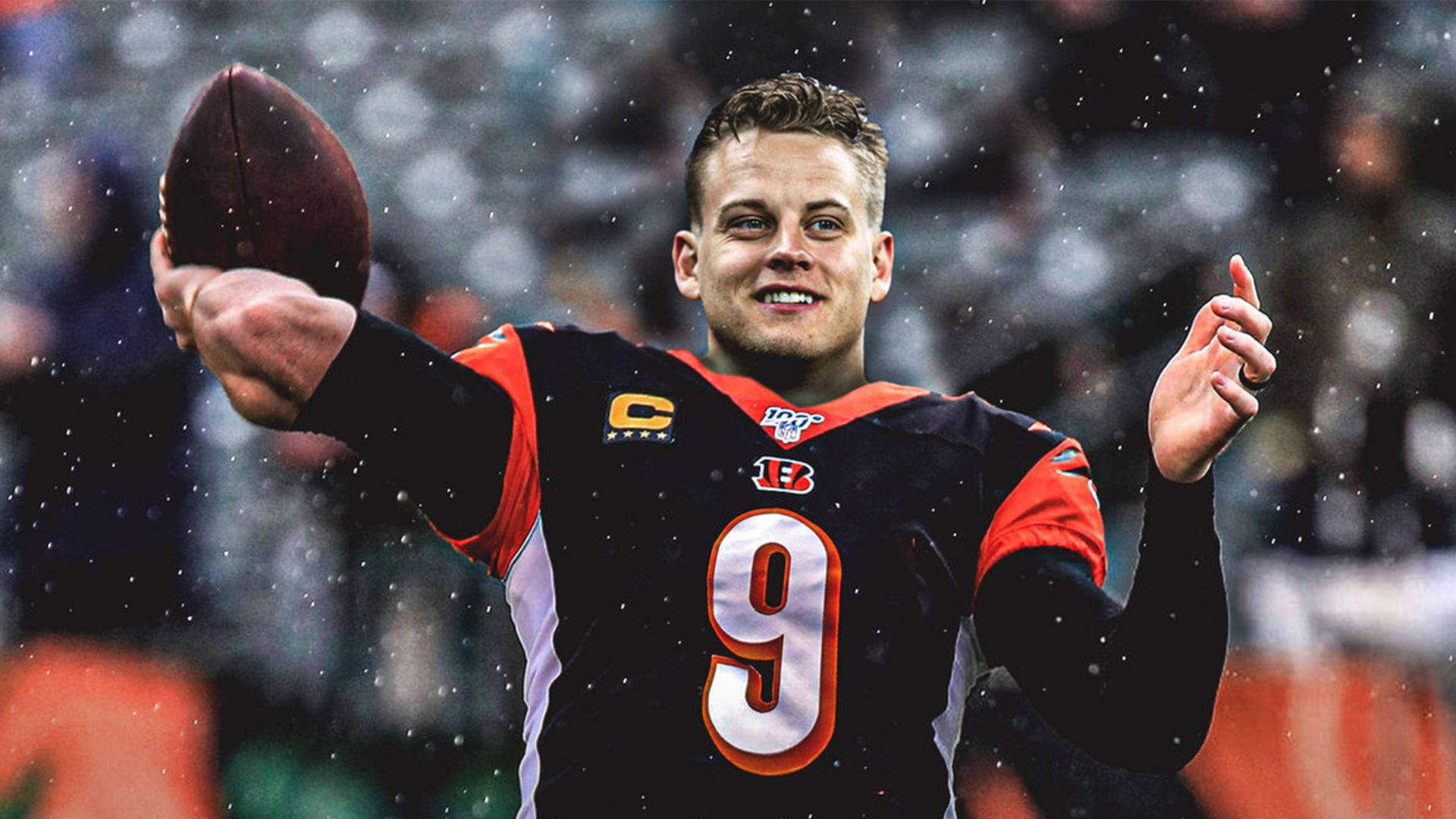 Joe Burrow 微笑投球 壁紙 — 一位微笑的美式足球四分衛身穿黑色和橙色9號球衣，在雨中拿著球並向上指。