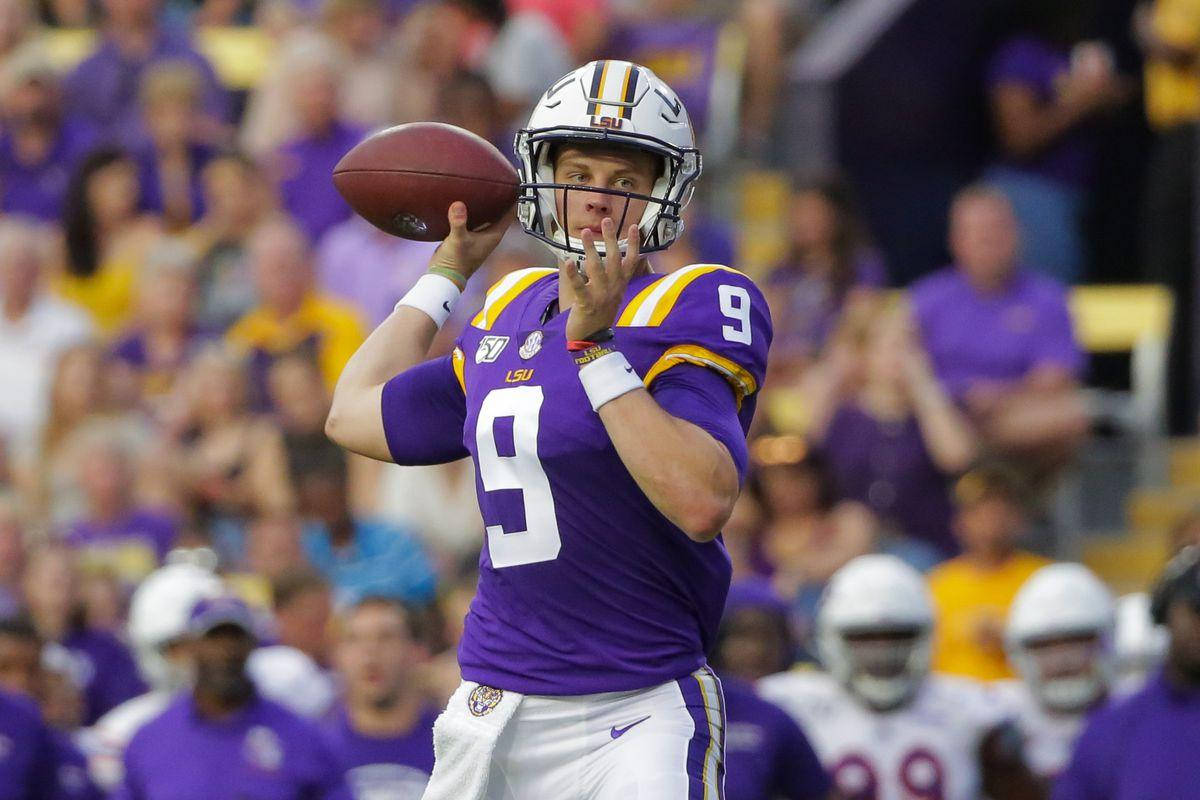 Joe Burrow 投球瞬間 壁紙 — 一名身穿紫色LSU 9號球衣的美式足球四分衛在比賽中準備傳球，背景是模糊的人群。
