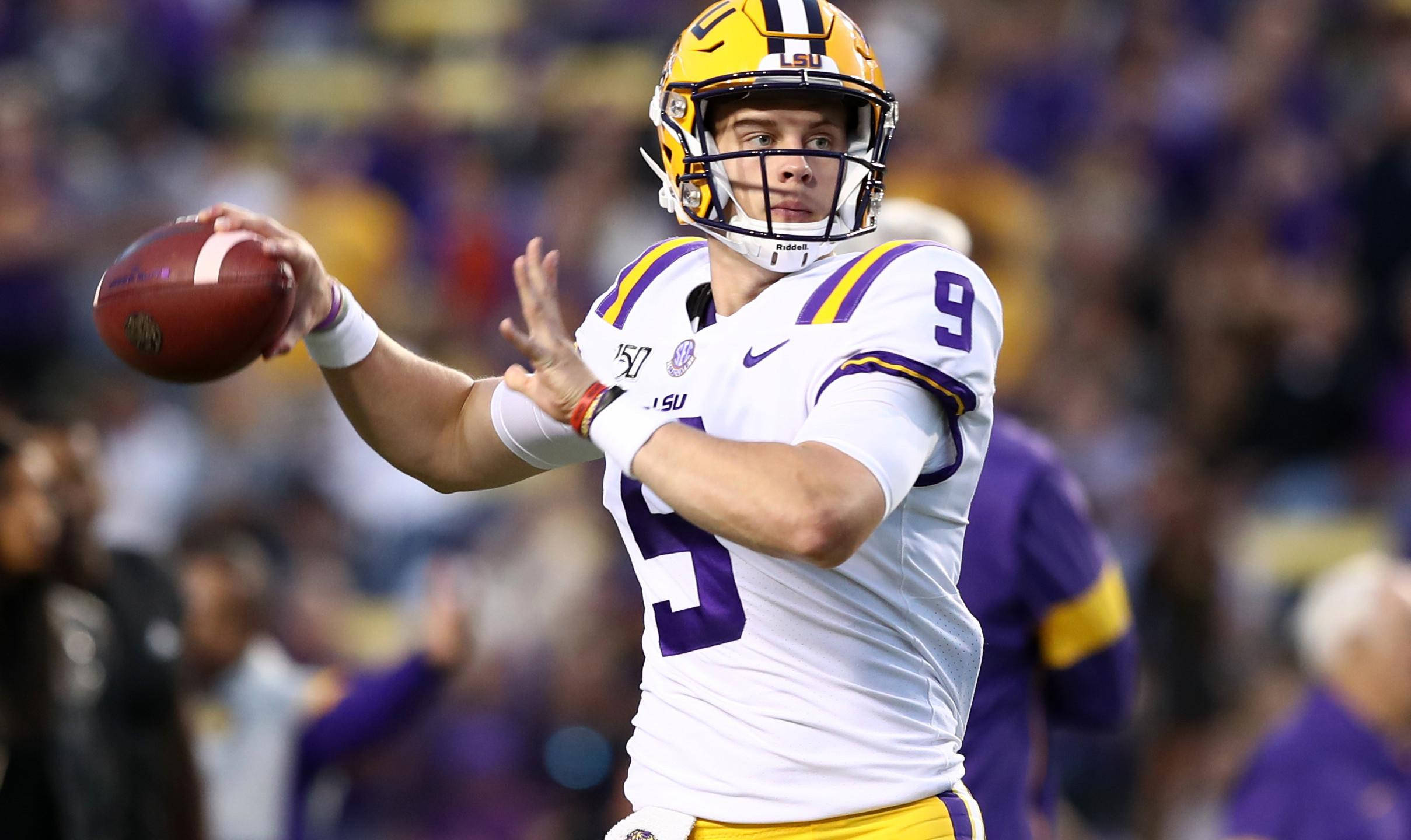 Joe Burrow 擲球揮臂 壁紙 — 一位專注的LSU美式足球四分衛穿著白色和紫色制服，在體育館燈光下的夜間比賽中投擲橄欖球。