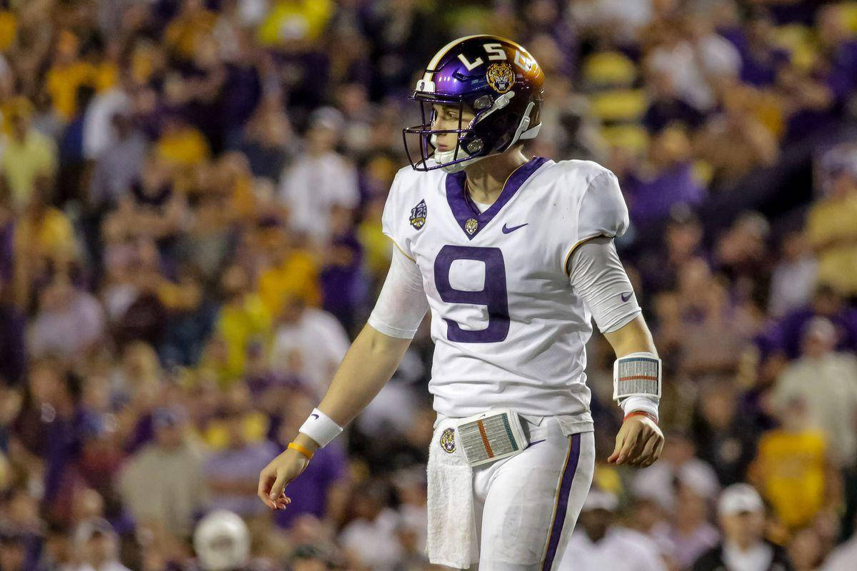 Joe Burrow 星級運動員 壁紙 — 一位專注的LSU美式足球四分衛，身穿白色和紫色9號球衣，站在球場上，體育場燈光下，背景是模糊的球迷。