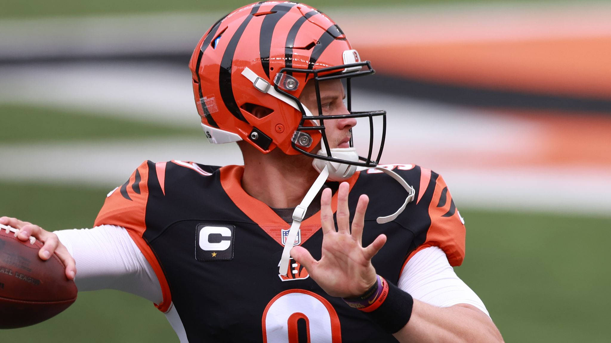 Joe Burrow 橙色頭盔 壁紙 — 辛辛那提猛虎隊的四分衛身穿黑色和橙色制服，準備在綠色場地上擲出橄欖球。
