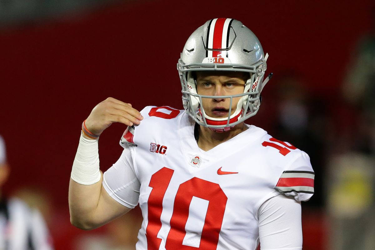 Joe Burrow 白色球衣 壁紙 — 一位專注的美式足球四分衛穿著白色和紅色制服，在體育場燈光下調整頭盔。