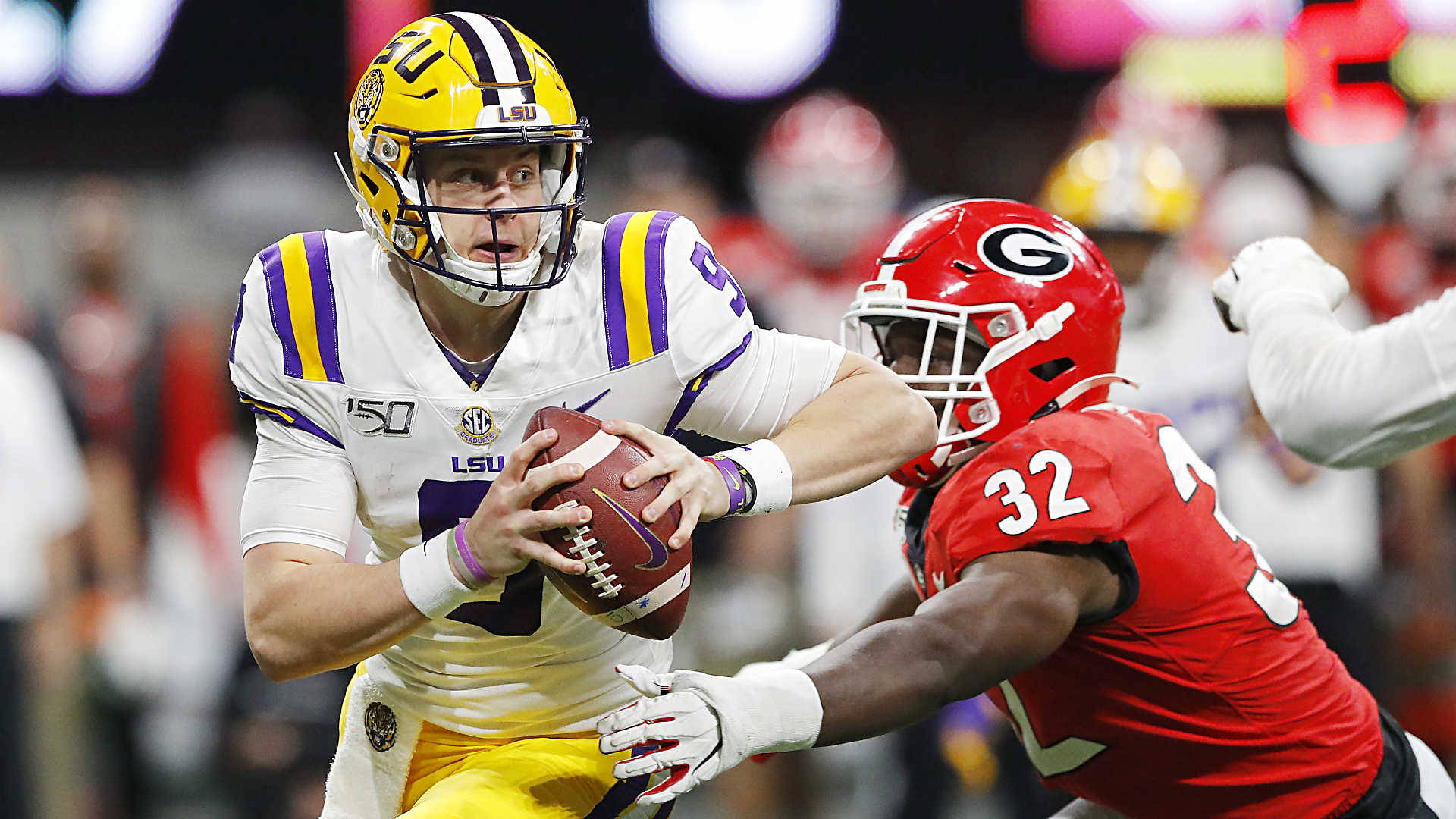 Joe Burrow 被擒抱 壁紙 — LSU四分衛戴著黃色頭盔、身穿白色球衣緊抱橄欖球，而佐治亞州紅色球衣的防守球員在夜間比賽中撲向他要擒抱。