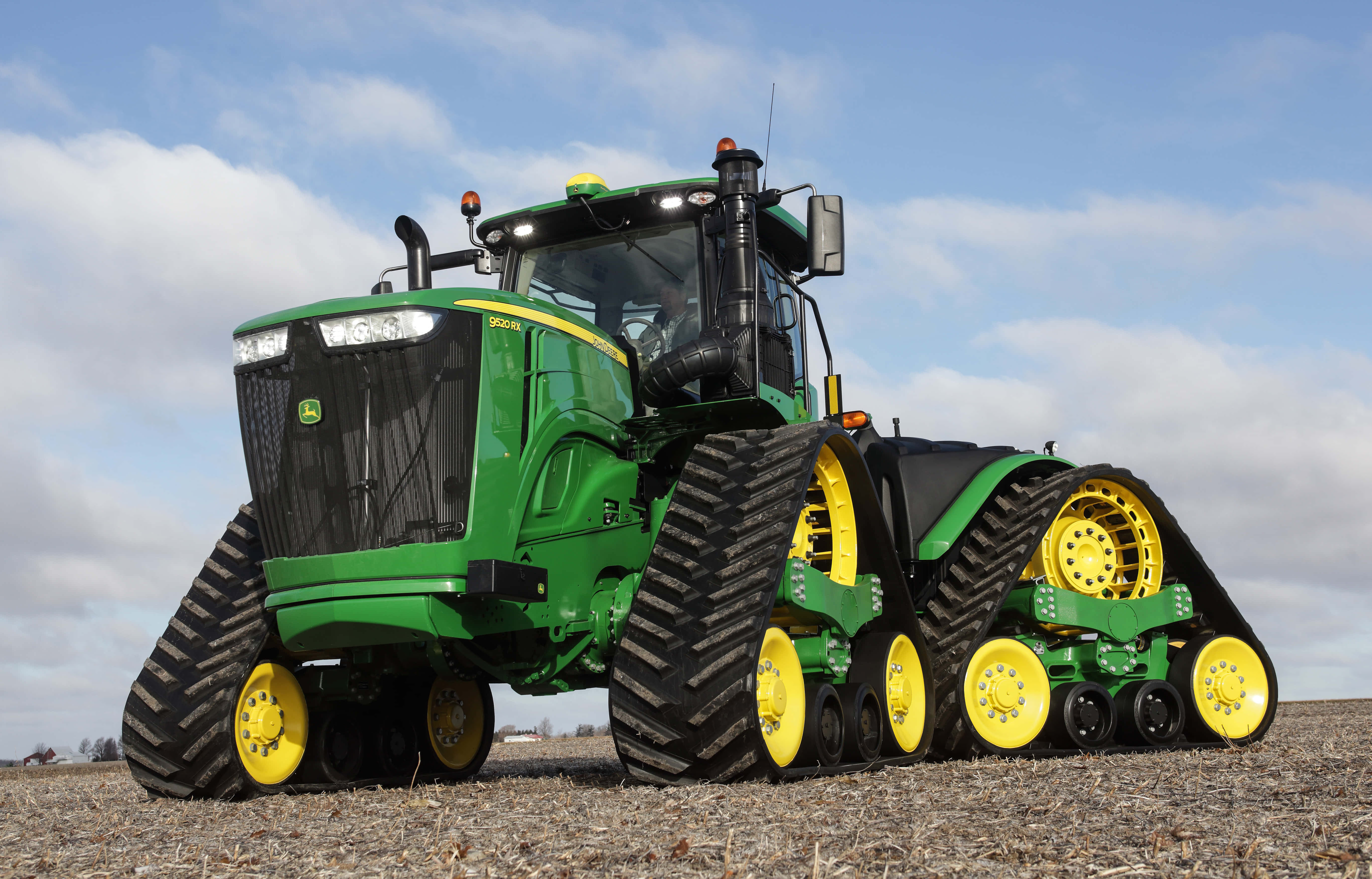 John Deere 最新款拖拉機圖片 壁紙 — 一部綠色和黃色的John Deere履帶拖拉機在陰天下的乾燥田野上強力地矗立。