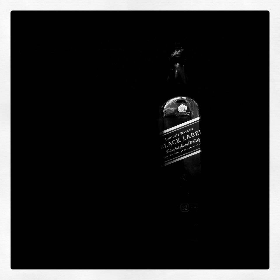 Johnnie Walker黑標 — 純粹奢華 壁紙 — 一瓶尊尼獲加黑牌威士忌在漆黑背景上以高對比度單色微弱發光。