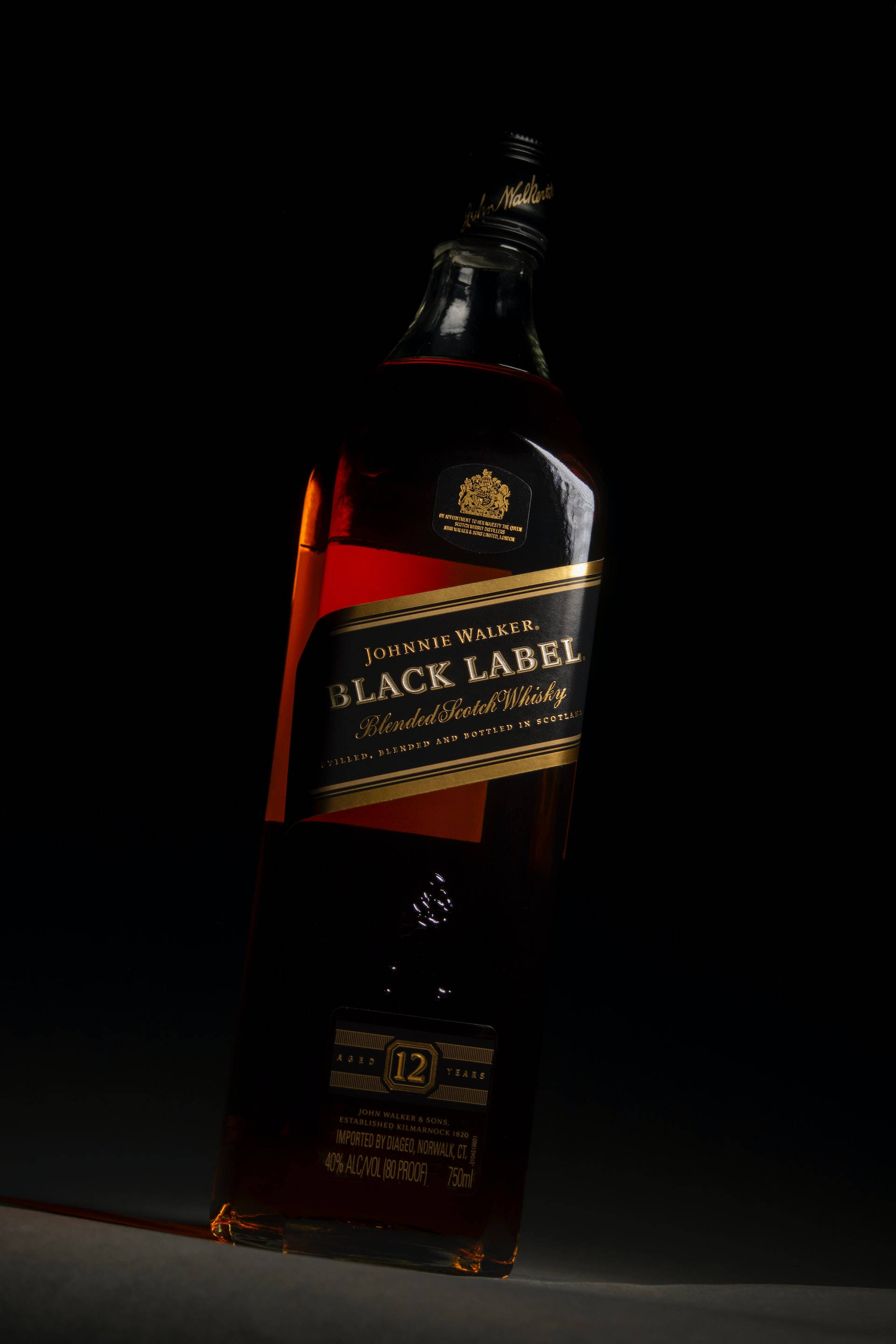 Johnnie Walker黑牌瓶身的典雅垂直壁紙 壁紙 — 時尚的Johnnie Walker Black Label威士忌酒瓶在純黑背景下閃耀著琥珀色液體。