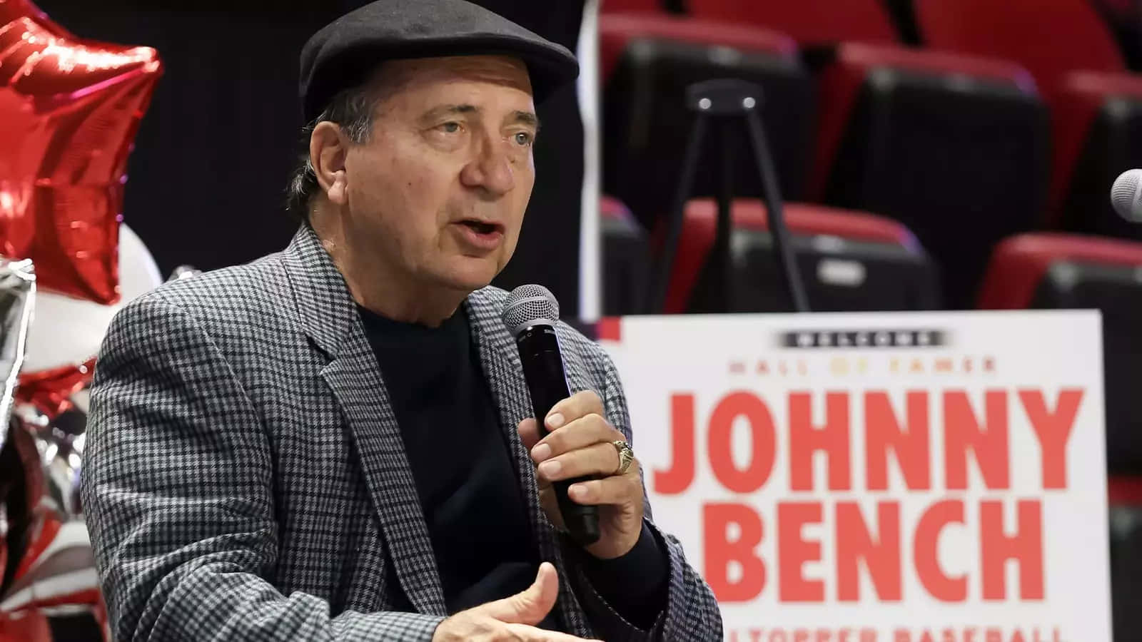  壁紙 — Johnny Bench 在名人堂入選活動中對著麥克風講話，身後有紅色氣球和體育場座位。