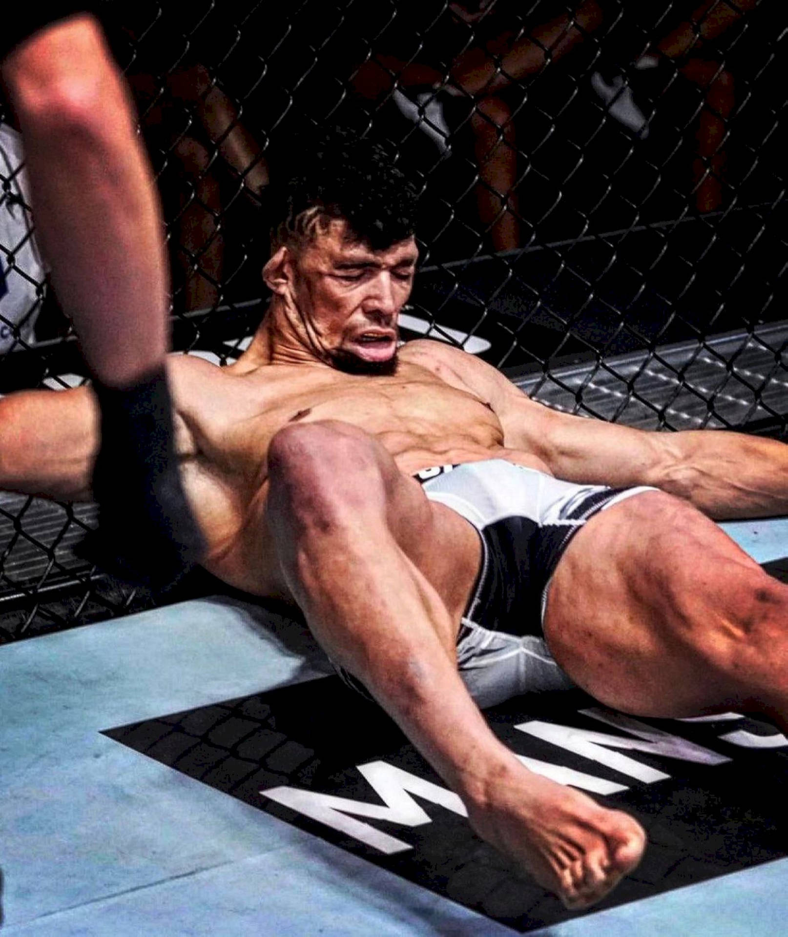 筋疲力竭的MMA拳手在激烈比賽後躺在八角籠墊子上。