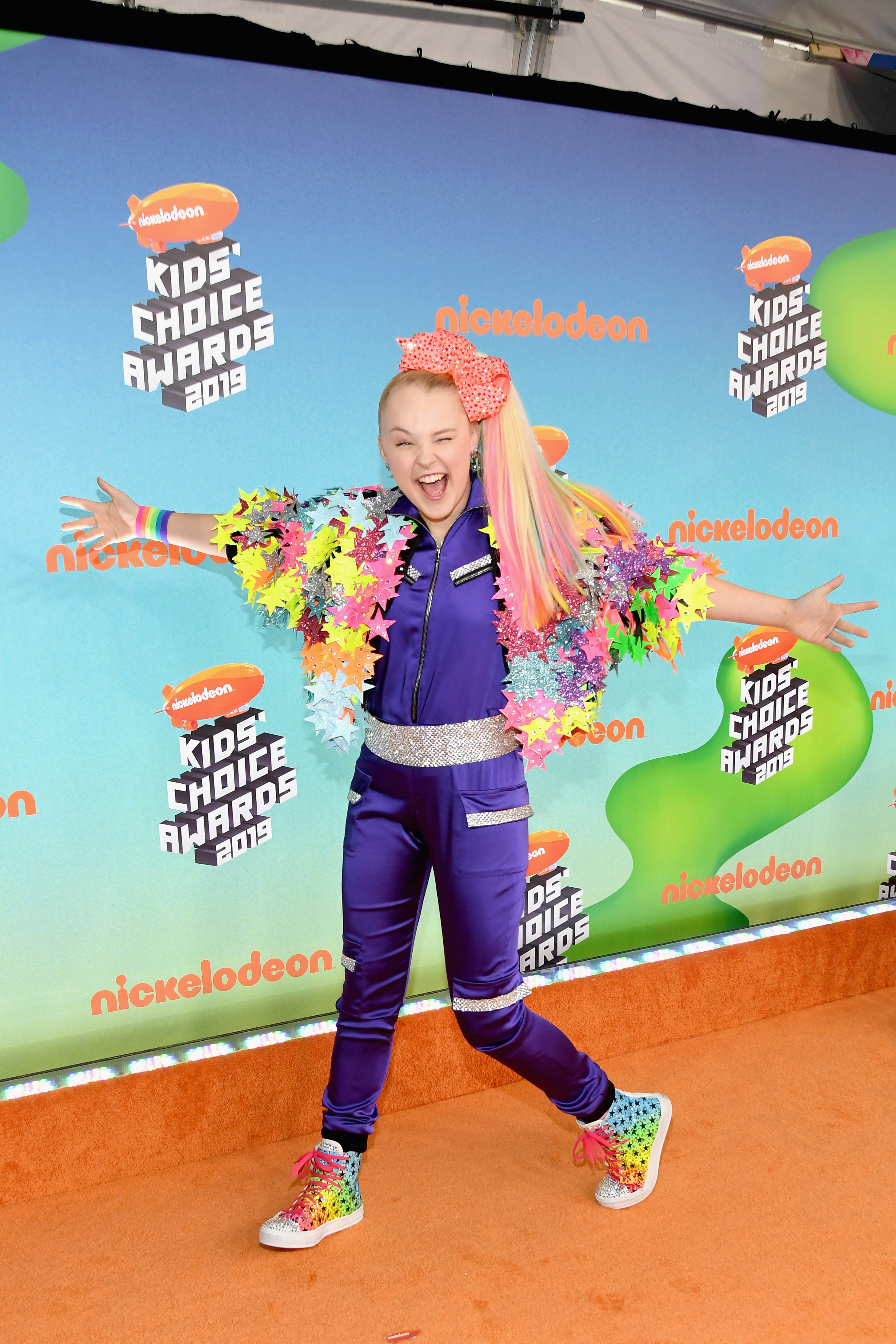 Jojo Siwa 出席 2015 年 Nickelodeon 兒童選擇獎 壁紙 — JoJo Siwa 喺2019年兒童選擇獎橙色地毯上，穿著鮮豔紫色服裝同彩虹配飾，擺出開心姿勢。