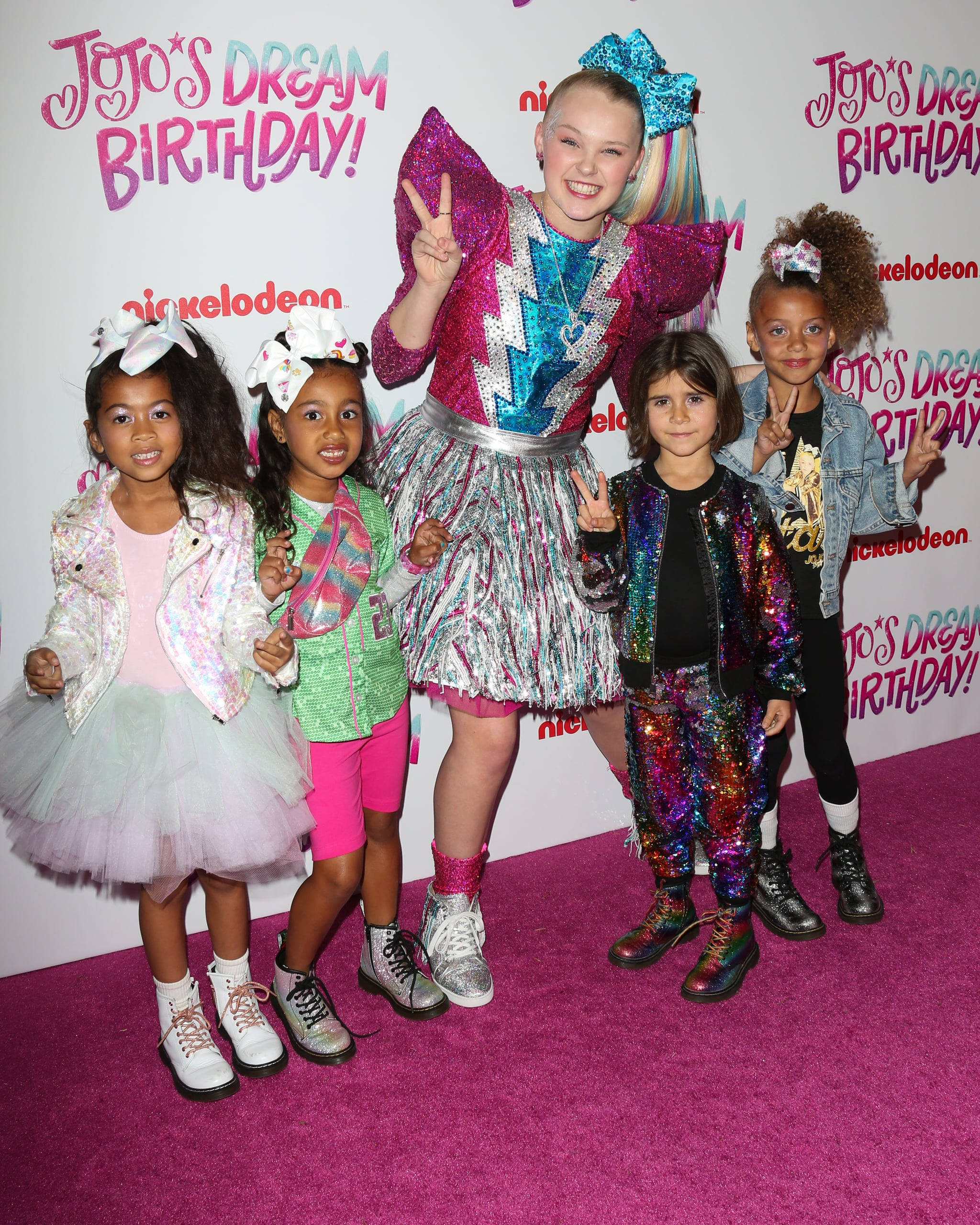 Jojo Siwa 與小朋友同框 壁紙 — 五個孩子穿著閃亮多彩的服裝，在Nickelodeon活動的粉紅色地毯上愉快地擺姿勢。