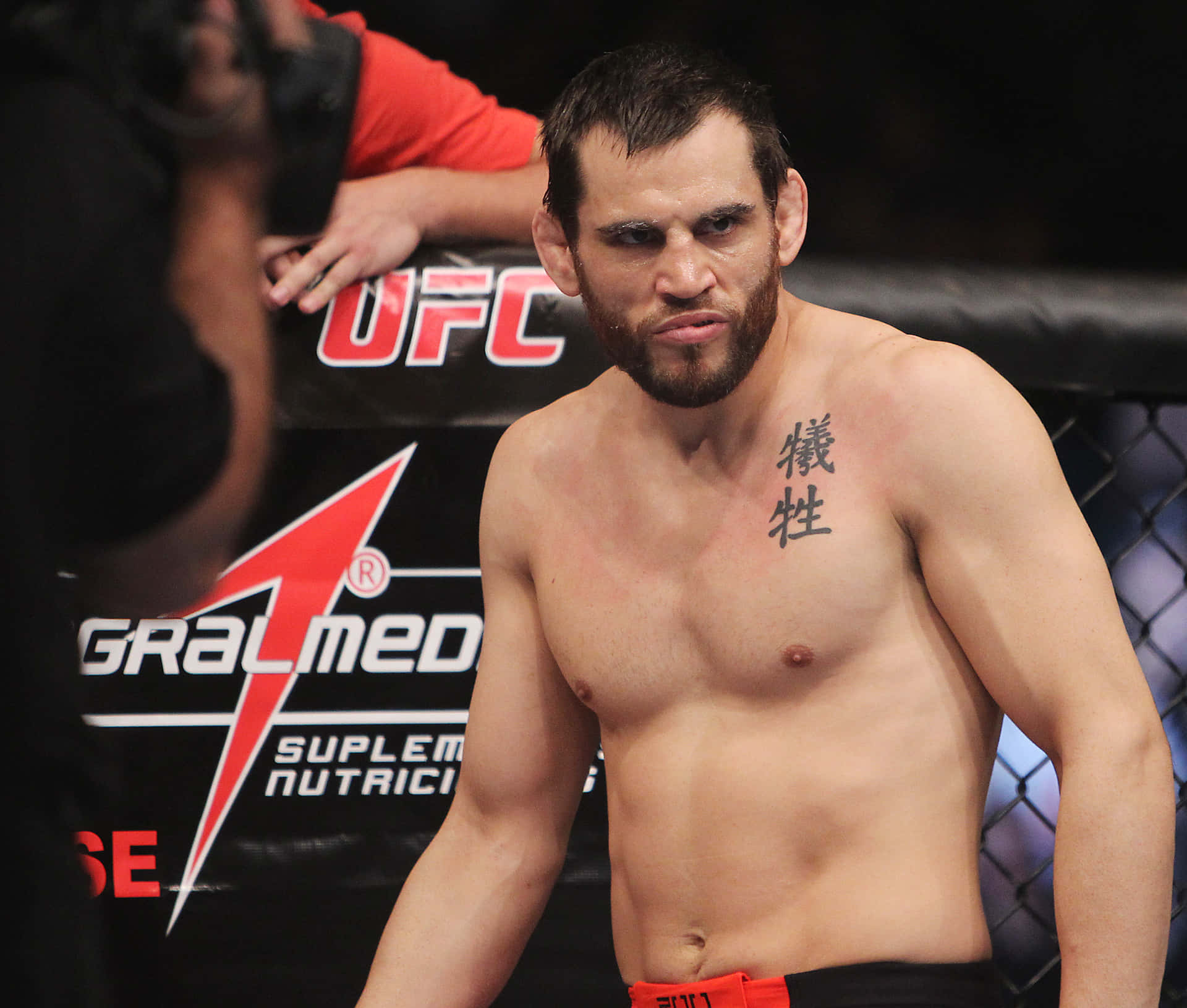 Jon Fitch於UFC 141賽事中眼神凌厲 壁紙 — 一位赤裸上身的UFC拳手，表情嚴肅，胸前紋有中文字，站在八角籠內。