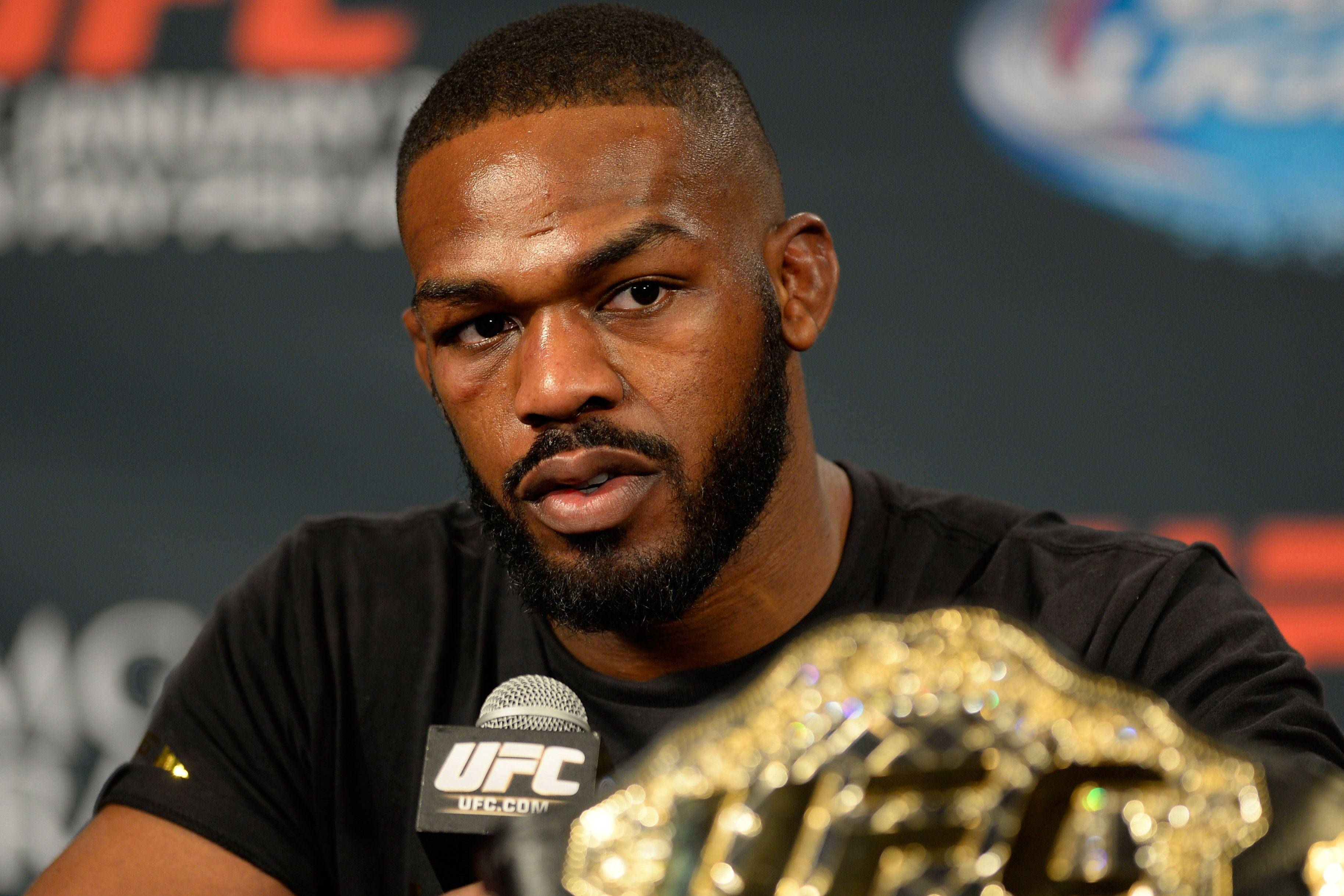Jon Jones 壓力會談現場 壁紙 — 一位專注的UFC拳手，在記者會上冠軍腰帶在他面前閃閃發光。