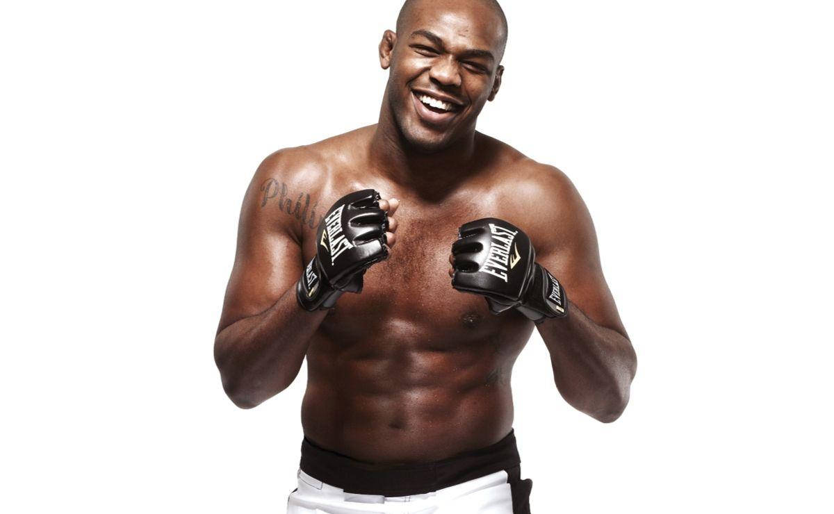 Jon Jones 專業攝影照 壁紙 — 一位肌肉發達的拳擊手戴著黑色手套，在純白背景前咧嘴大笑，展示他線條分明的體格和紋身。