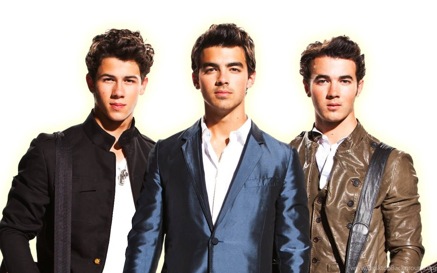 Jonas Brothers 2010 巡迴演唱會 壁紙 — 三位年輕男士身穿時尚外套，在明亮的白色背景前自信擺姿勢，配以柔和的金色燈光。