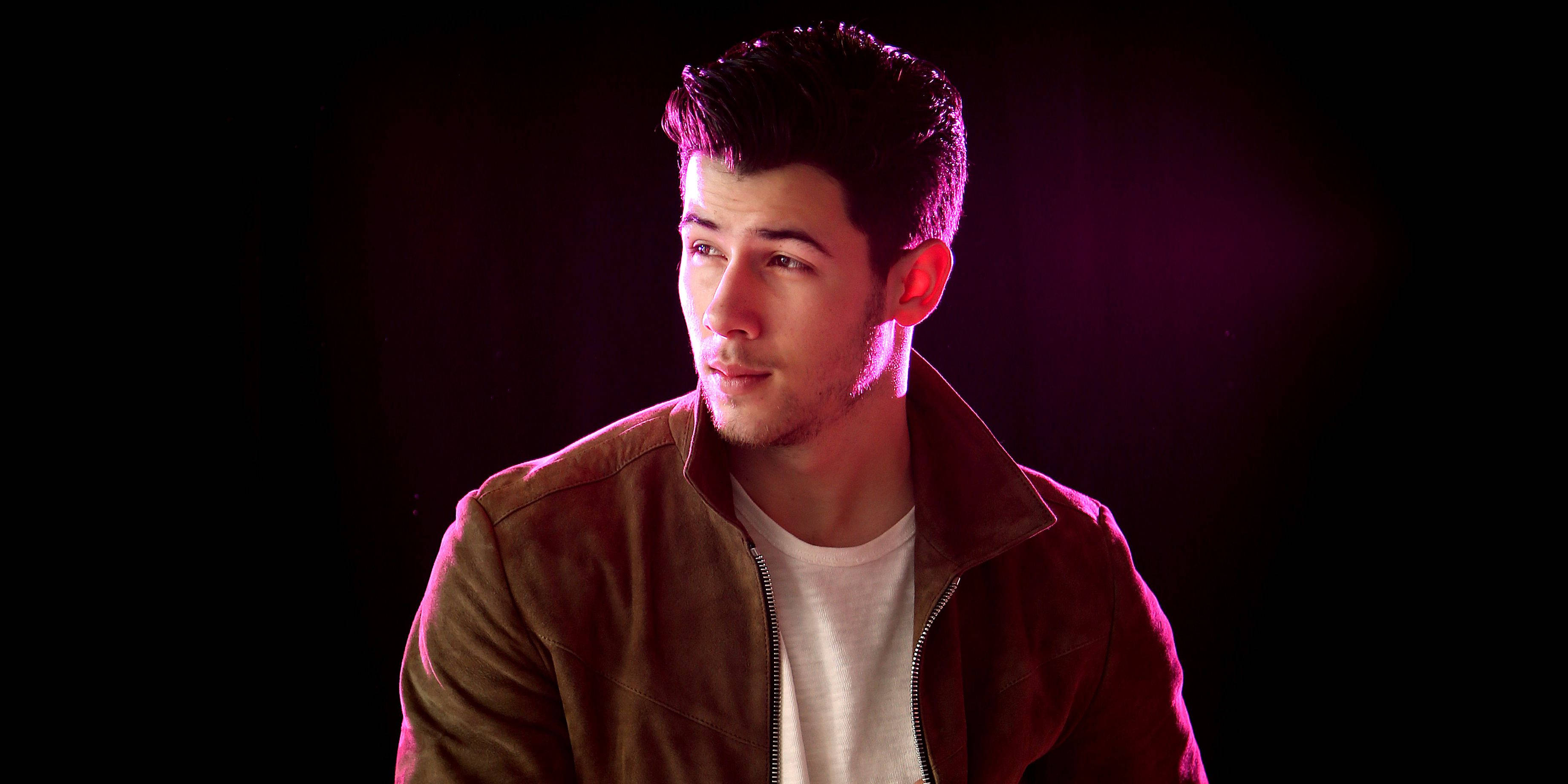 Jonas Brothers的Nick Jonas帥氣造型 壁紙 — 一個穿著棕色皮褸的男人，在充滿活力的洋紅色燈光下，對著黑暗的背景沉思地凝視。