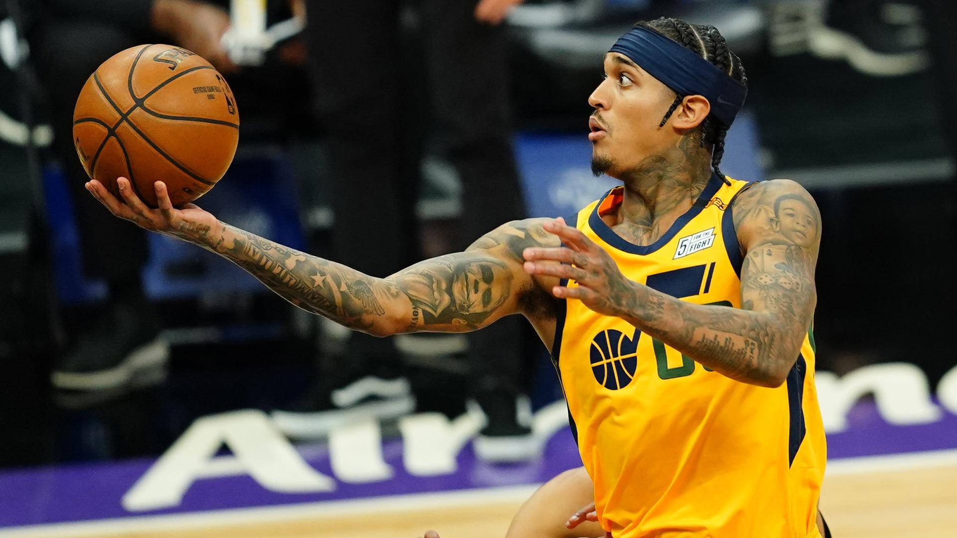 搞笑的Jordan Clarkson 壁紙 — 一位有紋身的籃球運動員身穿黃色球衣，在明亮的場館燈光下準備在激烈的比賽中傳球。
