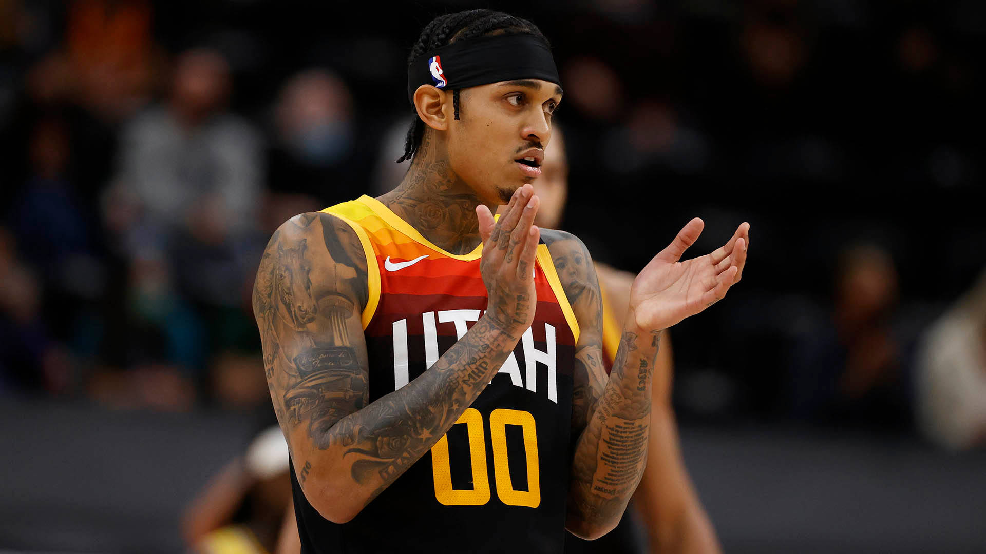 Jordan Clarkson緩慢鼓掌 壁紙 — 一位身上有紋身的籃球運動員，身穿猶他爵士隊球衣，在場館燈光下的比賽中難以置信地拍手。