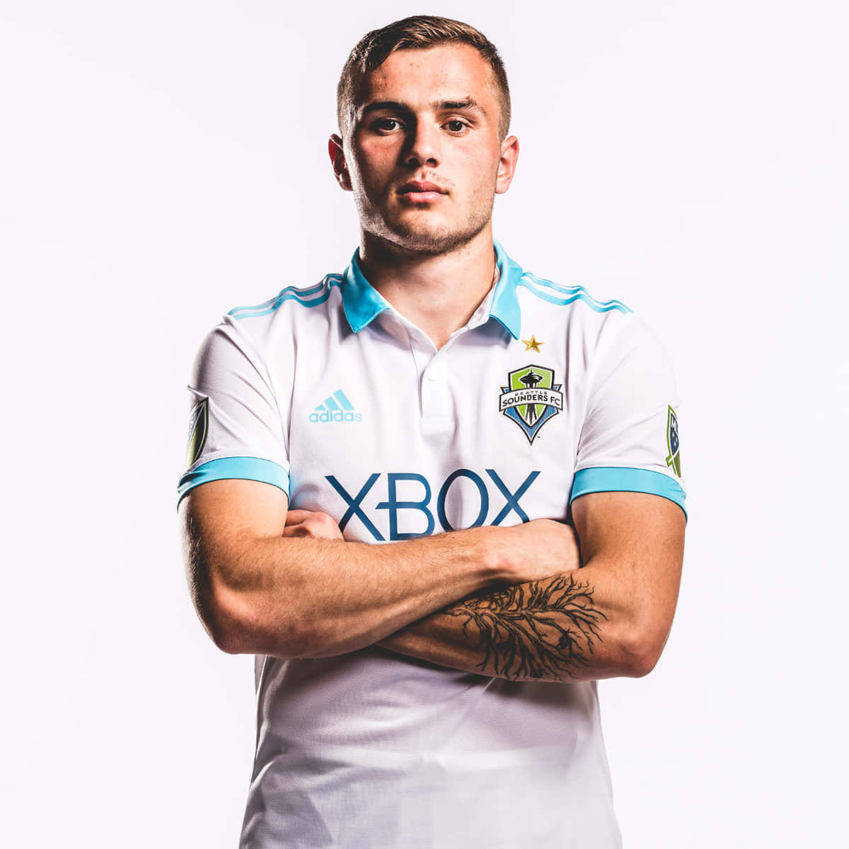 Jordan Morris 2016 年 Adidas 客場球衣 壁紙 — 一位自信的足球員身穿白色和青綠色的西雅圖海灣者FC球衣，在純白色背景前交叉雙臂站立。