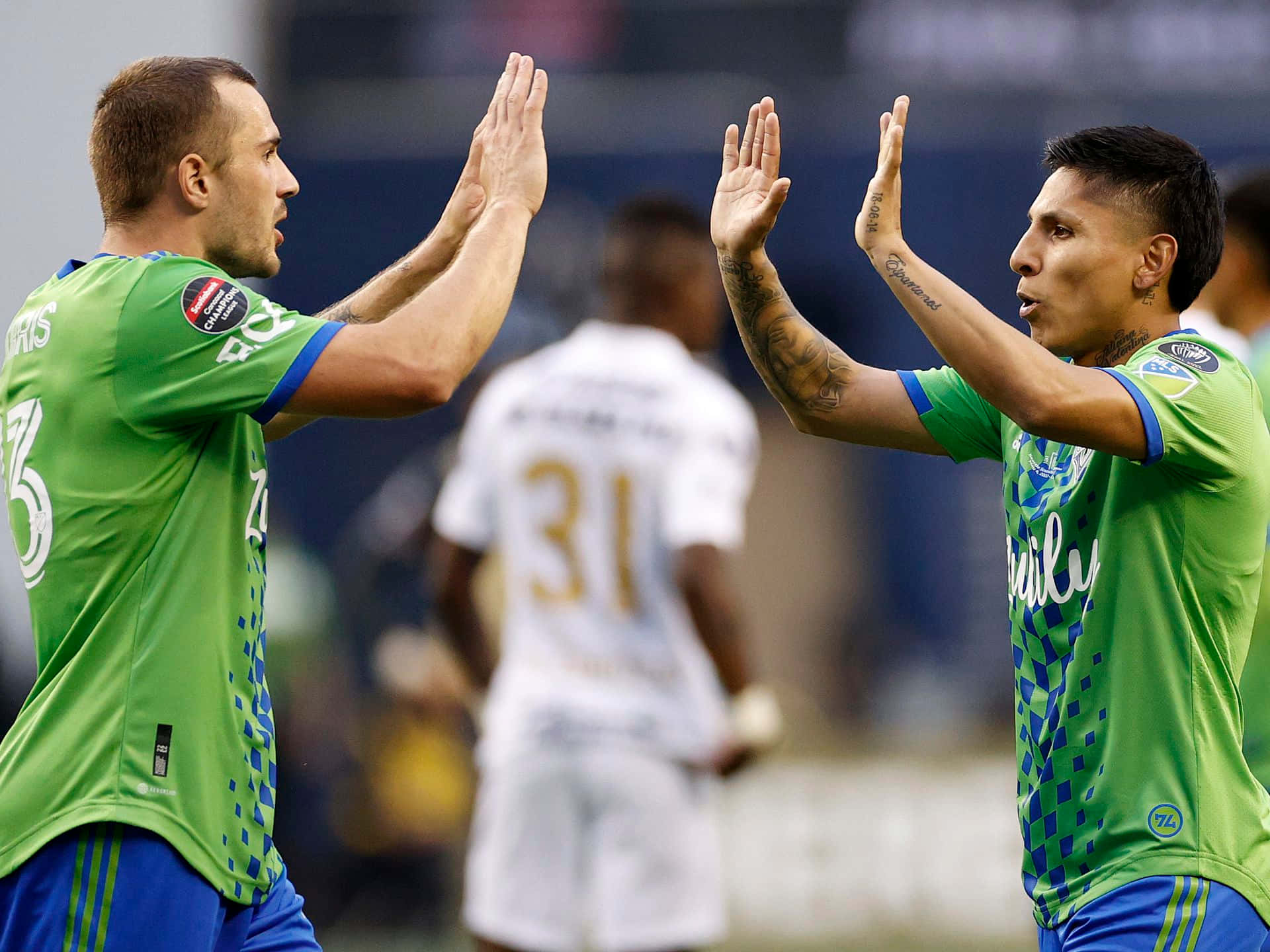 Jordan Morris 與 Raúl Ruidíaz 2022 西雅圖音速隊慶祝 壁紙 — 兩名身穿綠色球衣的足球運動員在體育場場地上擊掌，身後有一名身穿白色球衣的模糊對手。
