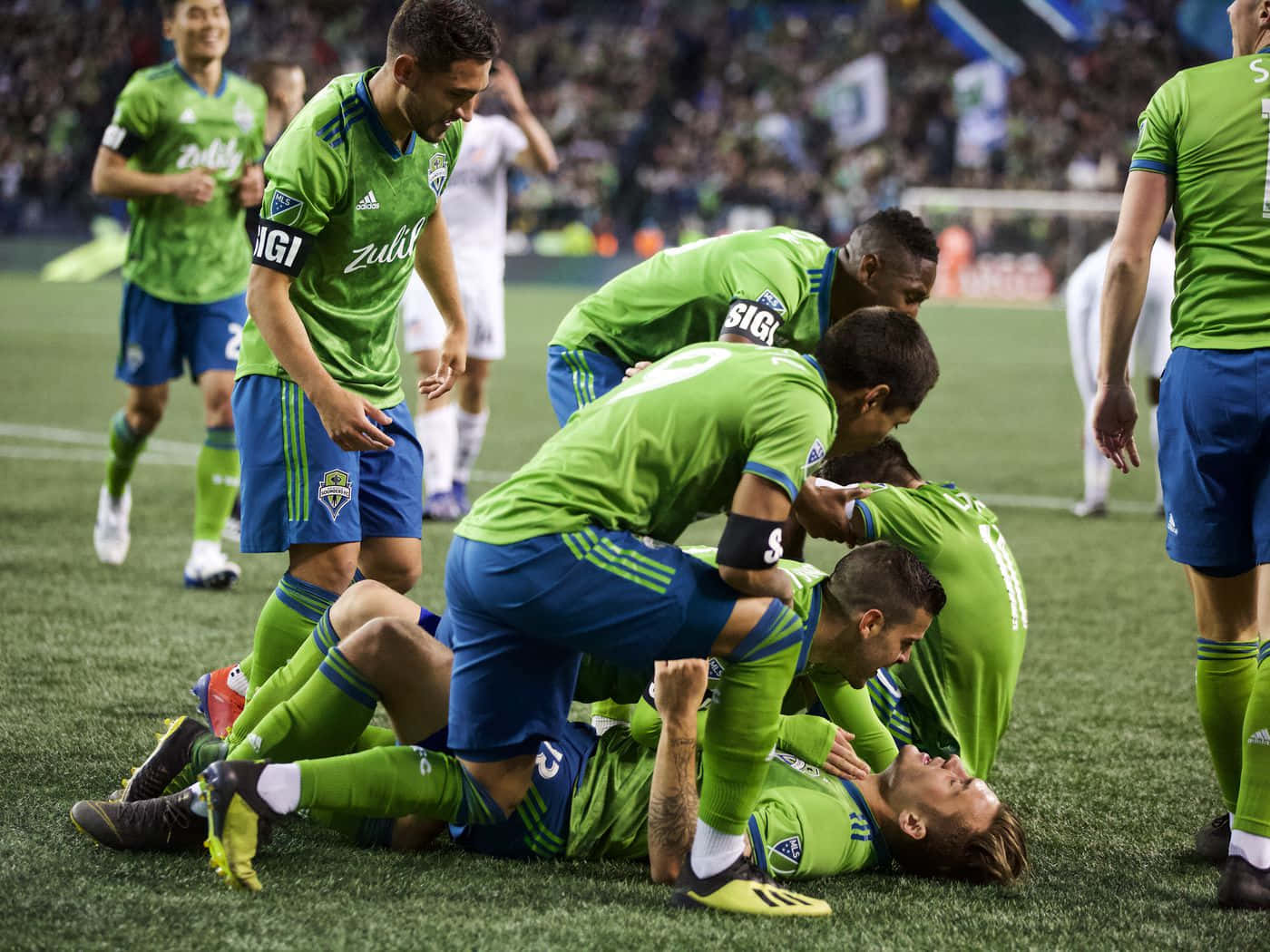 Jordan Morris 與西雅圖音速隊隊友慶祝 2019 年 MLS 总決賽進球 壁紙 — 穿著綠色球衣的足球運動員在球場草地上入球後疊在隊友身上。