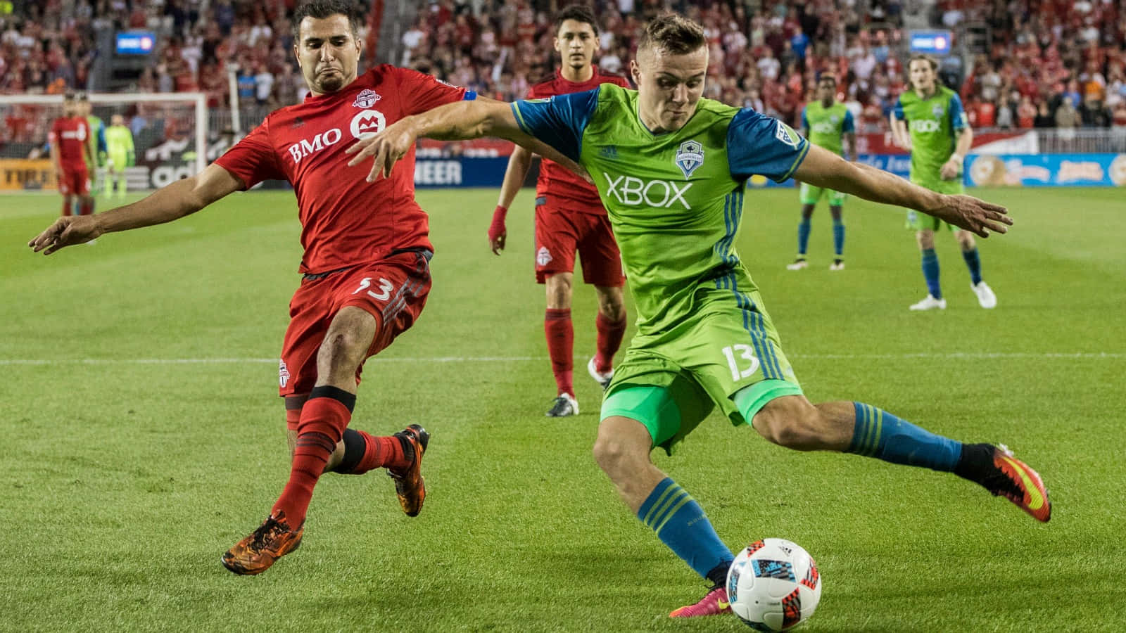 Jordan Morris 西雅圖音速隊對陣多倫多FC 2022 壁紙 — 兩名身穿紅色和綠色球衣的足球員在體育場燈光下，於充滿活力的綠色球場上激烈爭奪控球權。