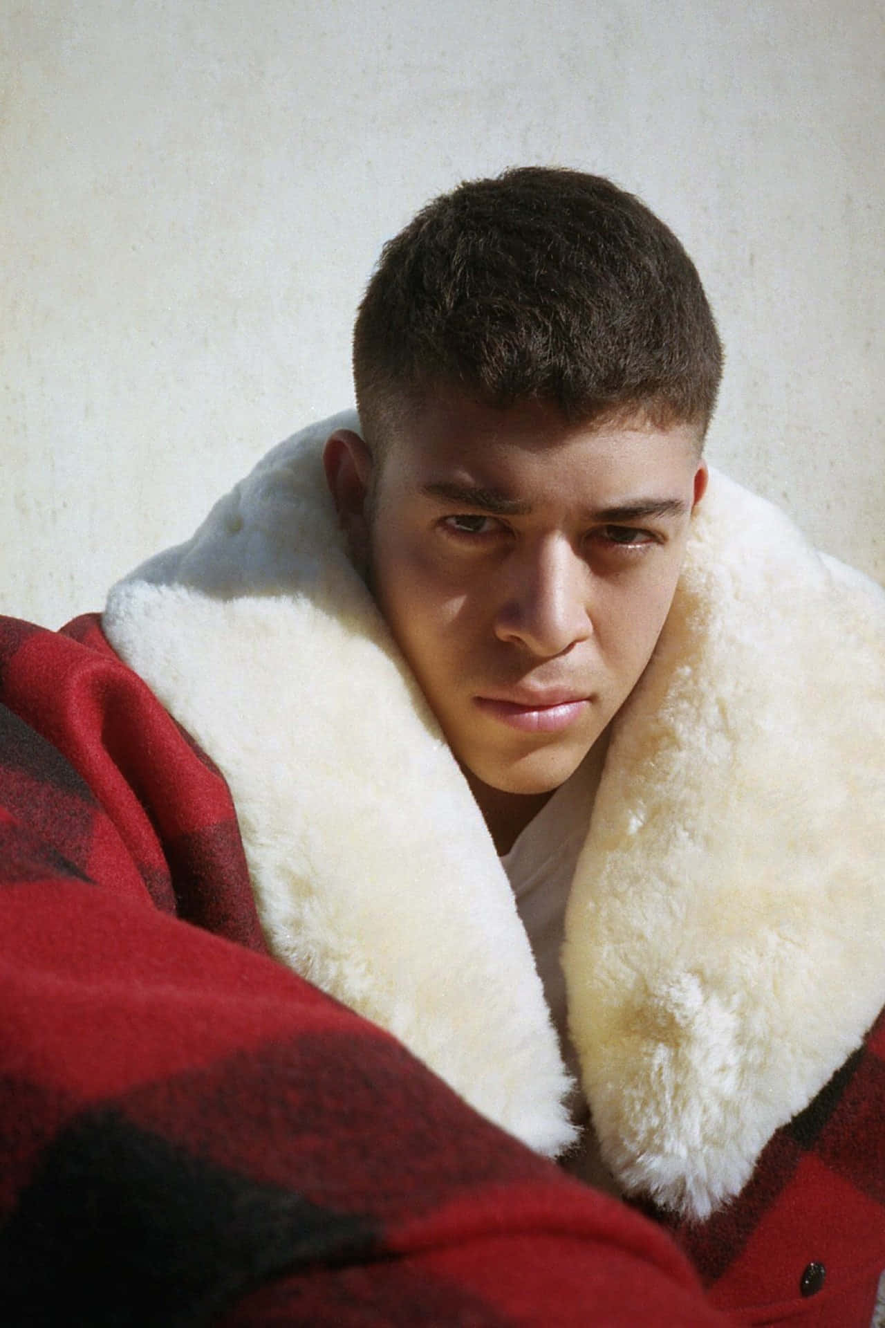 熱血少年Jordan為Vogue 2016專題拍攝 壁紙 — 一個短黑髮的年輕男子，裹著一條有毛茸茸白色領子的紅色格仔毯，專注地凝視著。