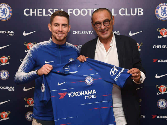 Jorge Luiz Frello Filho 持著 Maurizio Sarri 球衣 壁紙 — 兩名男子微笑著，在品牌背景前舉起一件藍色車路士足球會球衣。