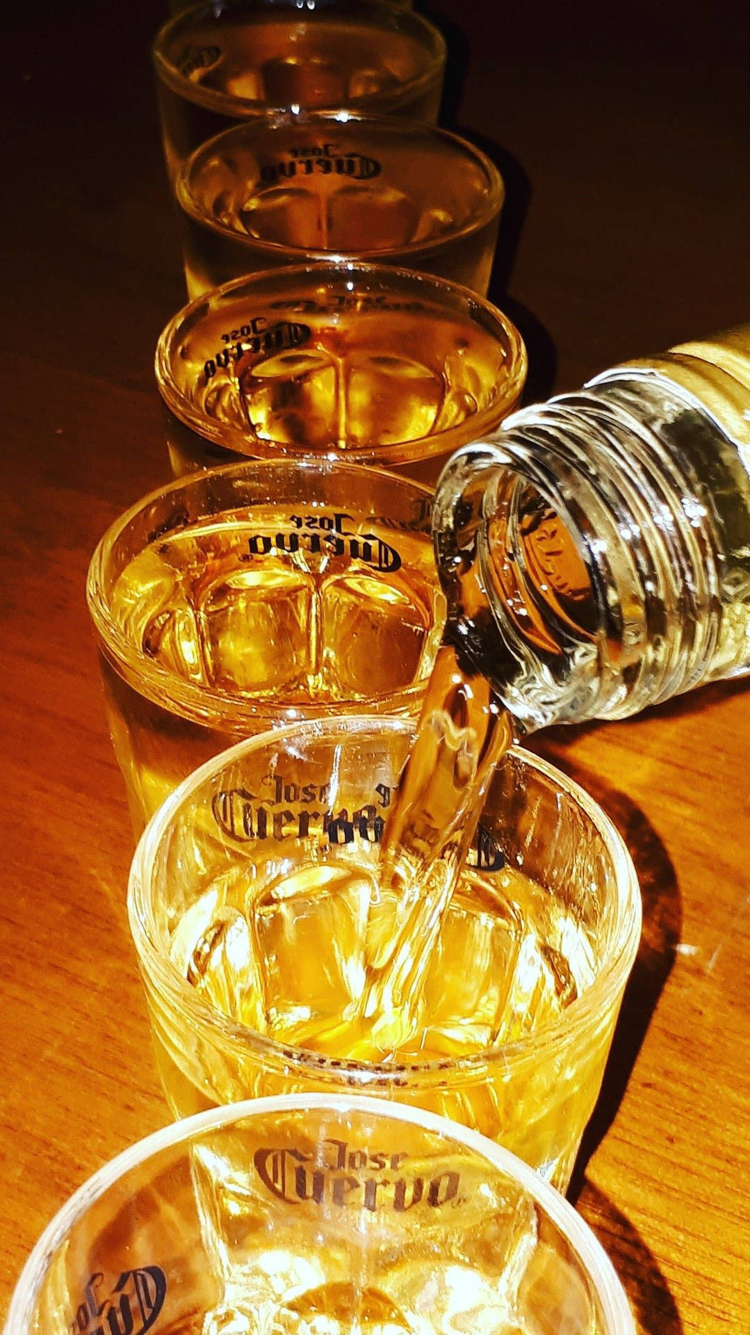 龍舌蘭酒被倒入木桌上裝有冰塊的品牌玻璃杯中。