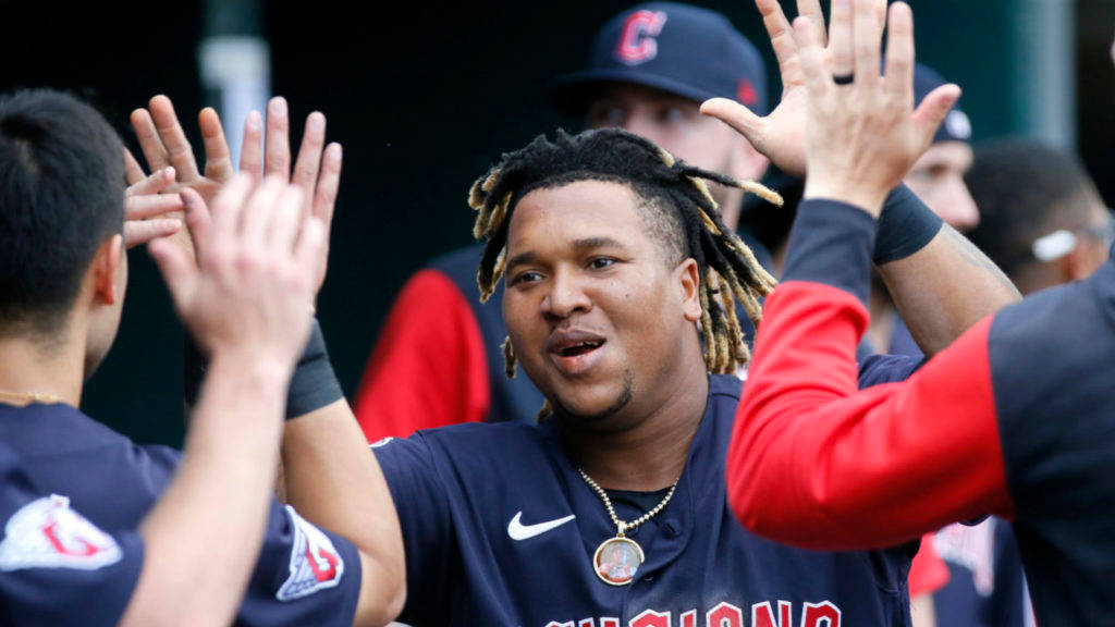 Jose Ramirez 克里夫蘭隊伍 壁紙 — 戴著辮子的棒球運動員在休息區與隊友擊掌，身穿帶有紅色點綴的海軍藍球衣。
