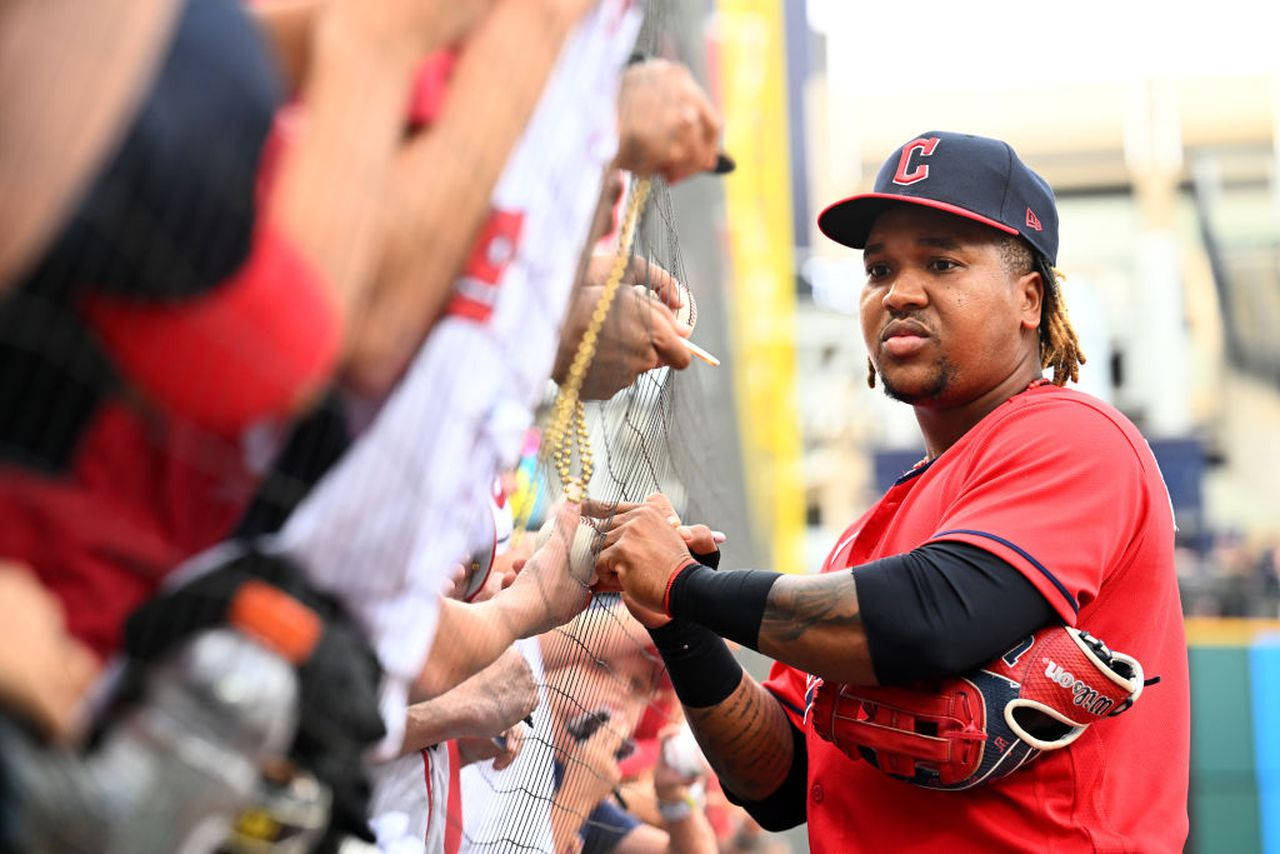 Jose Ramirez 粉絲簽名照 壁紙 — 一位身穿紅色球衣的棒球運動員在陽光明媚的日子裡，透過體育館的保護網為球迷簽名。